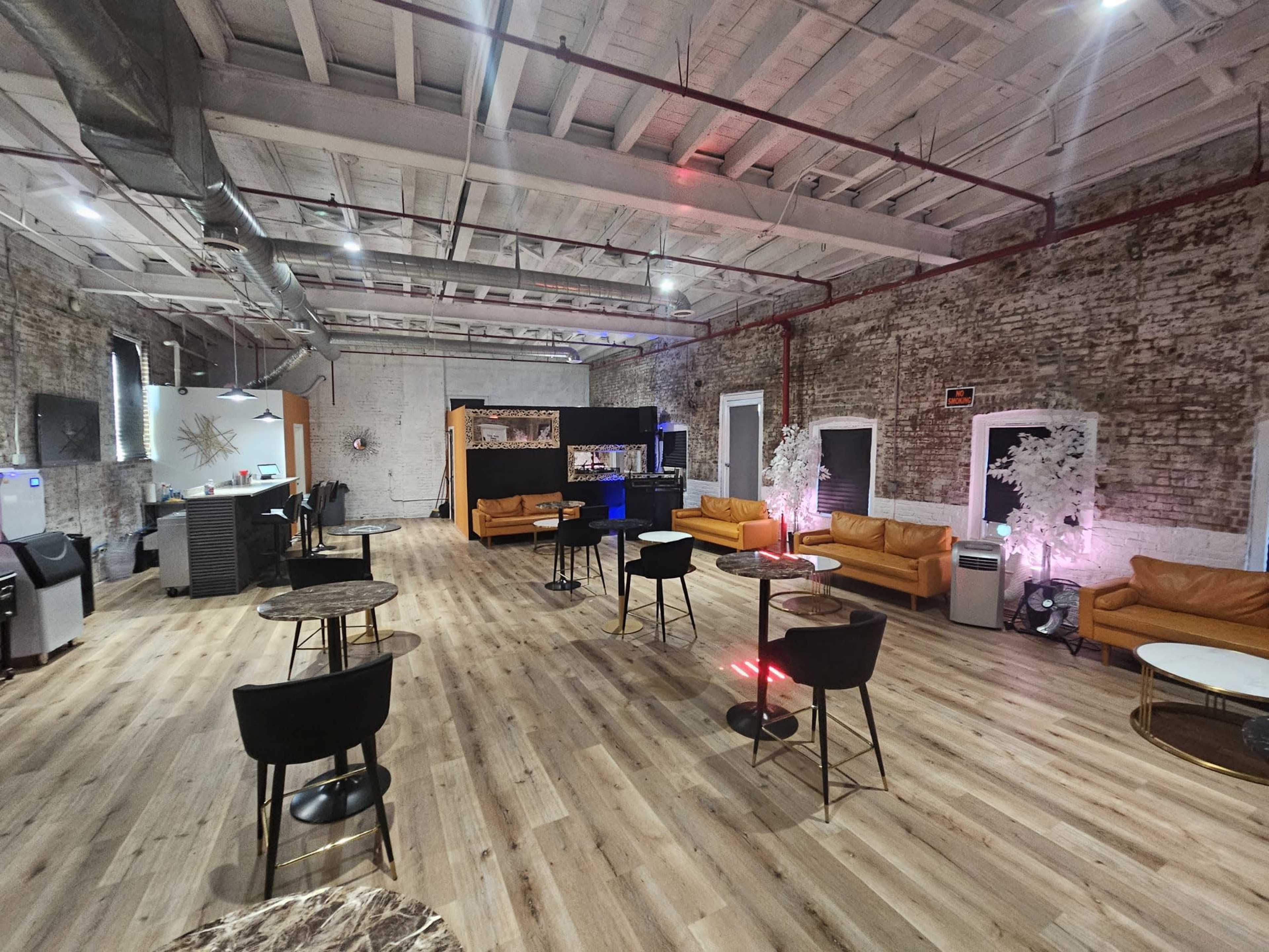 An industrial-style event space with exposed brick walls, wooden floors, and several seating areas featuring orange couches and small tables.