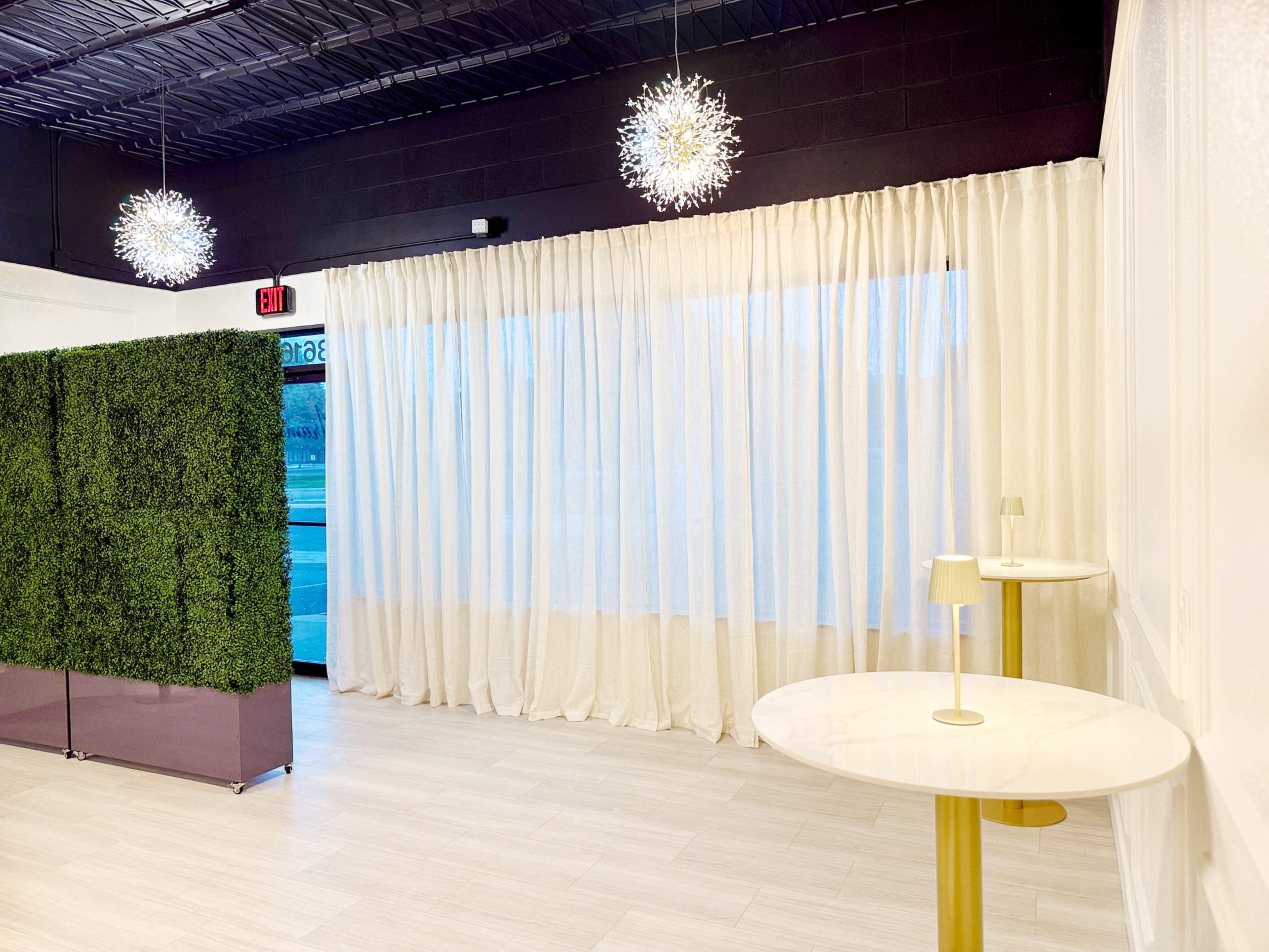 The image shows a modern interior space with two round tables, a green decorative wall, and two pendant light fixtures hanging from the ceiling.