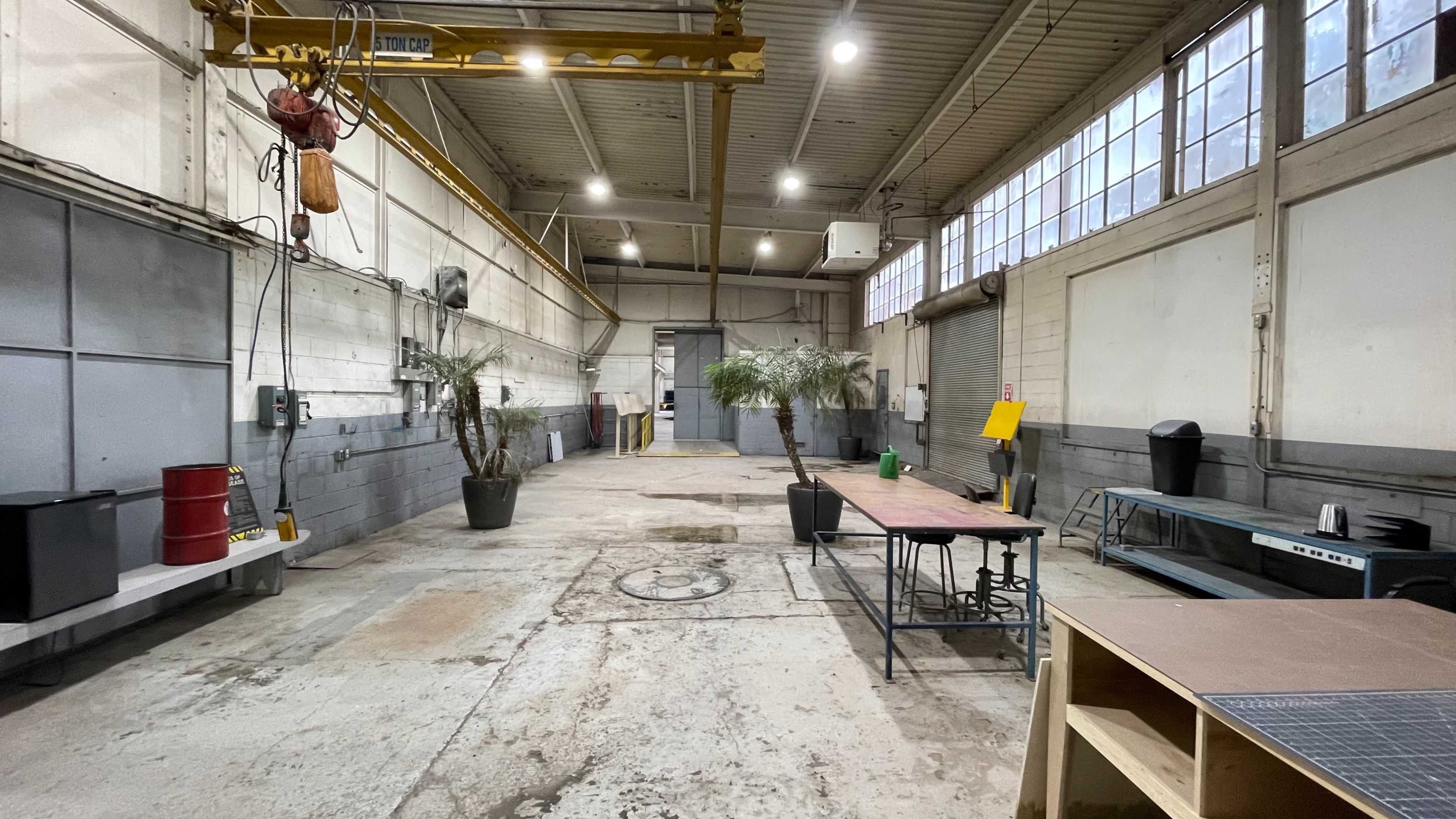 The image depicts an industrial warehouse interior with concrete floors, large windows, and various pieces of equipment arranged throughout the space.
