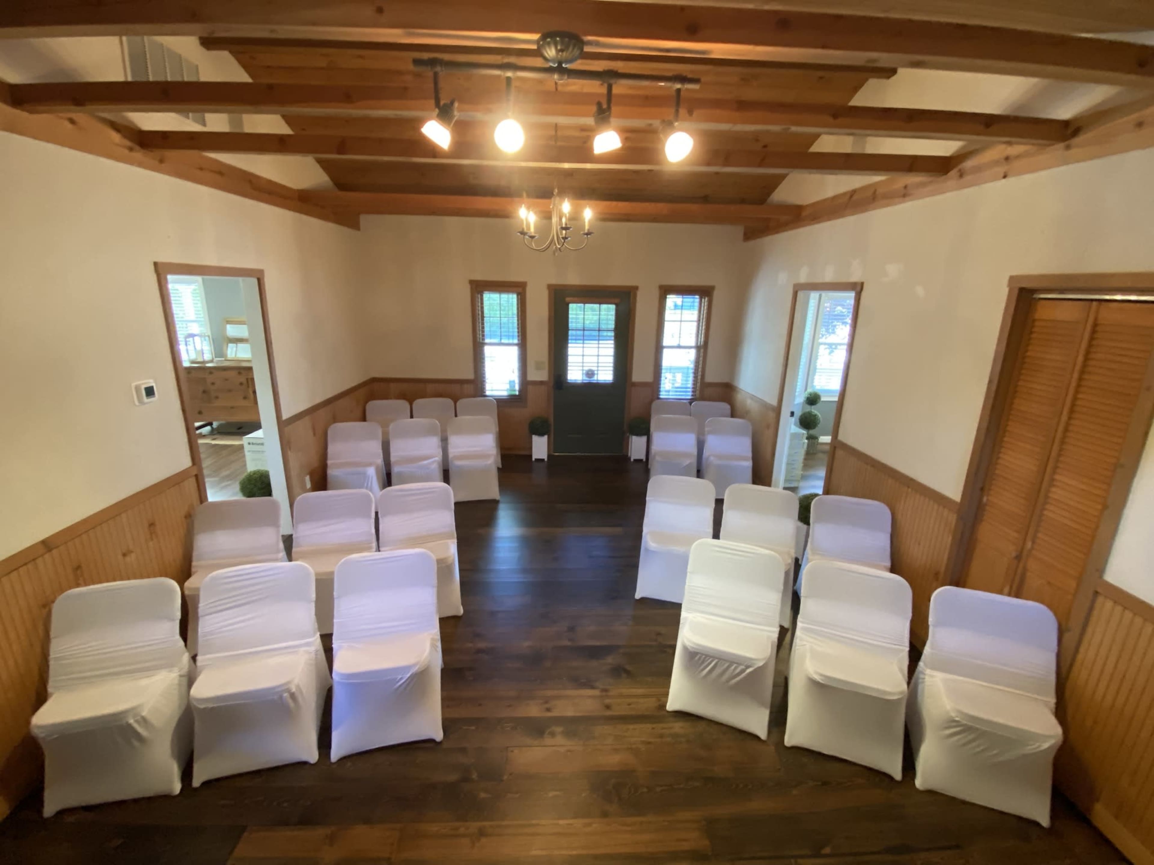 The image shows a room set up for an event with neatly arranged rows of white-covered chairs facing a green door.