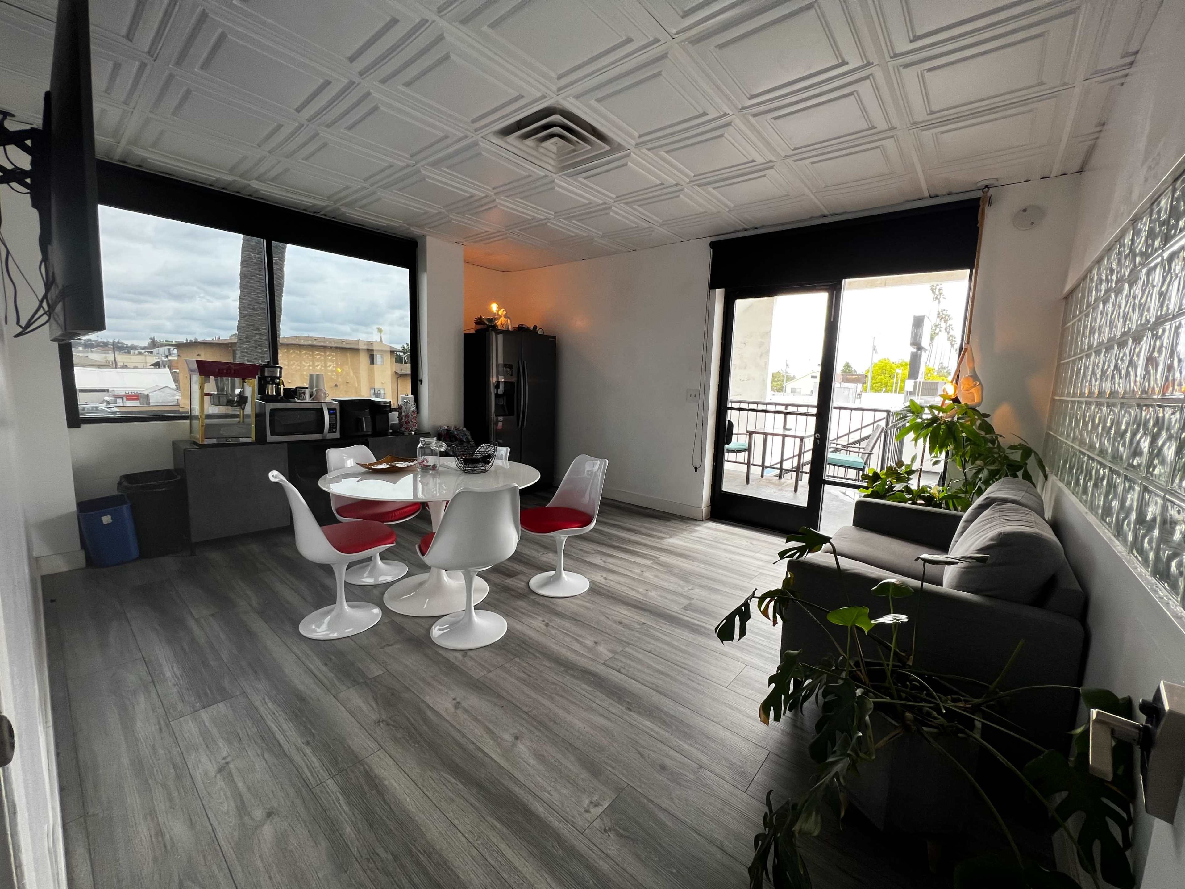 A modern dining area features a round table with white chairs, a gray sofa, and large windows overlooking an outdoor space.