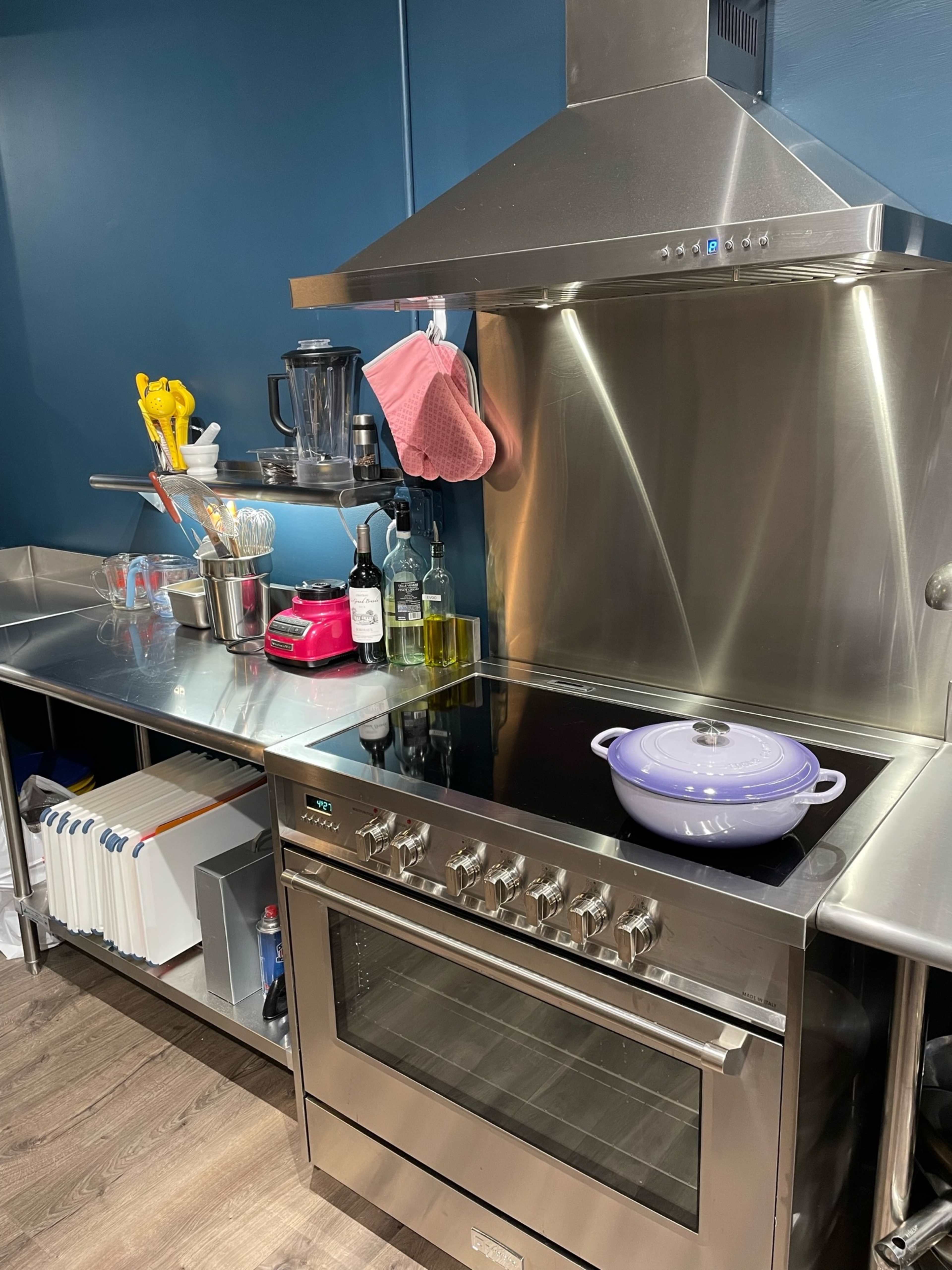 The image shows a modern kitchen with stainless steel appliances, a blue wall, and various cooking utensils organized on the countertop.