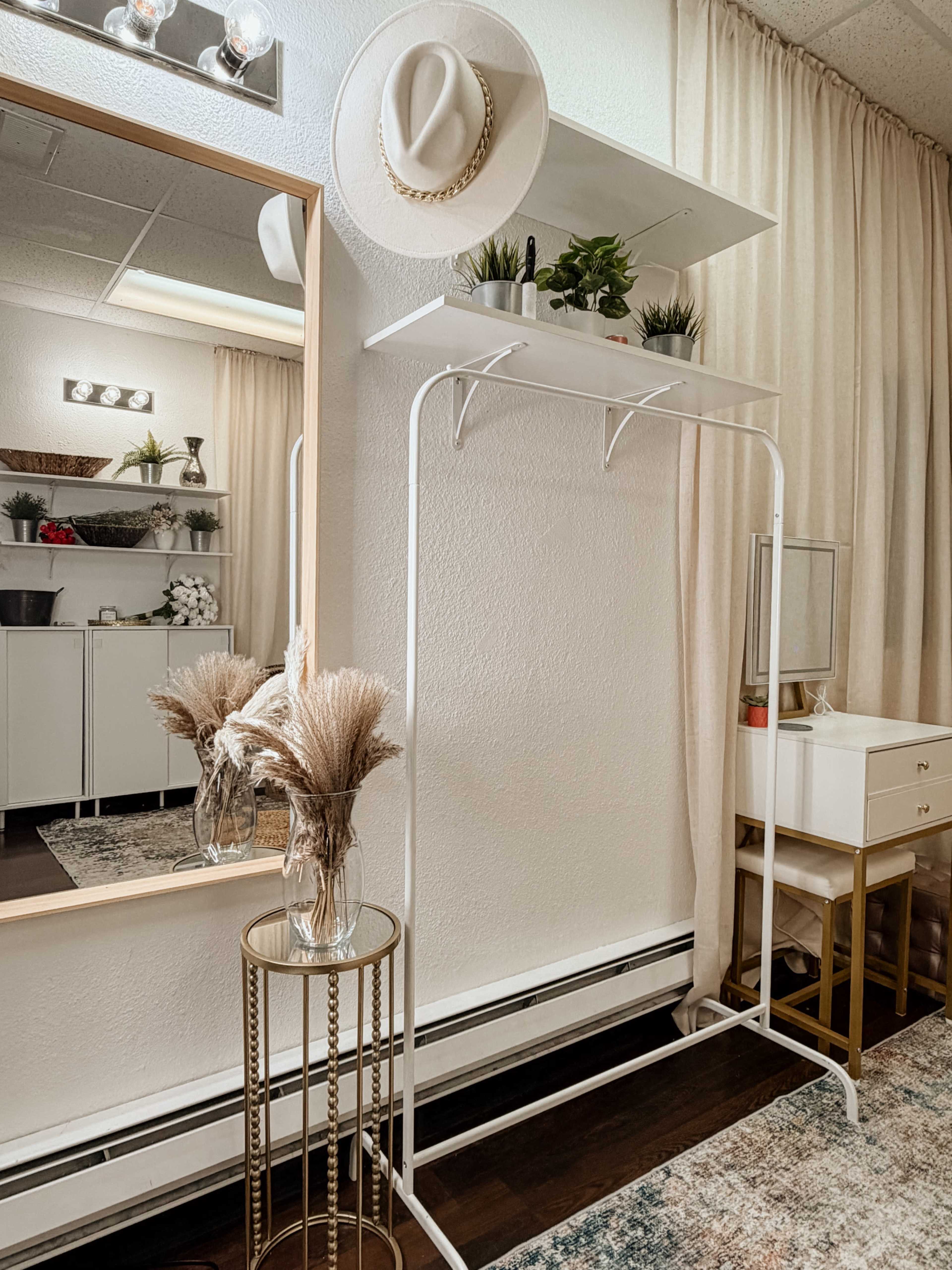 The image features a stylish dressing area with a white garment rack, a mirror, and decorative items on shelves and a tabletop.