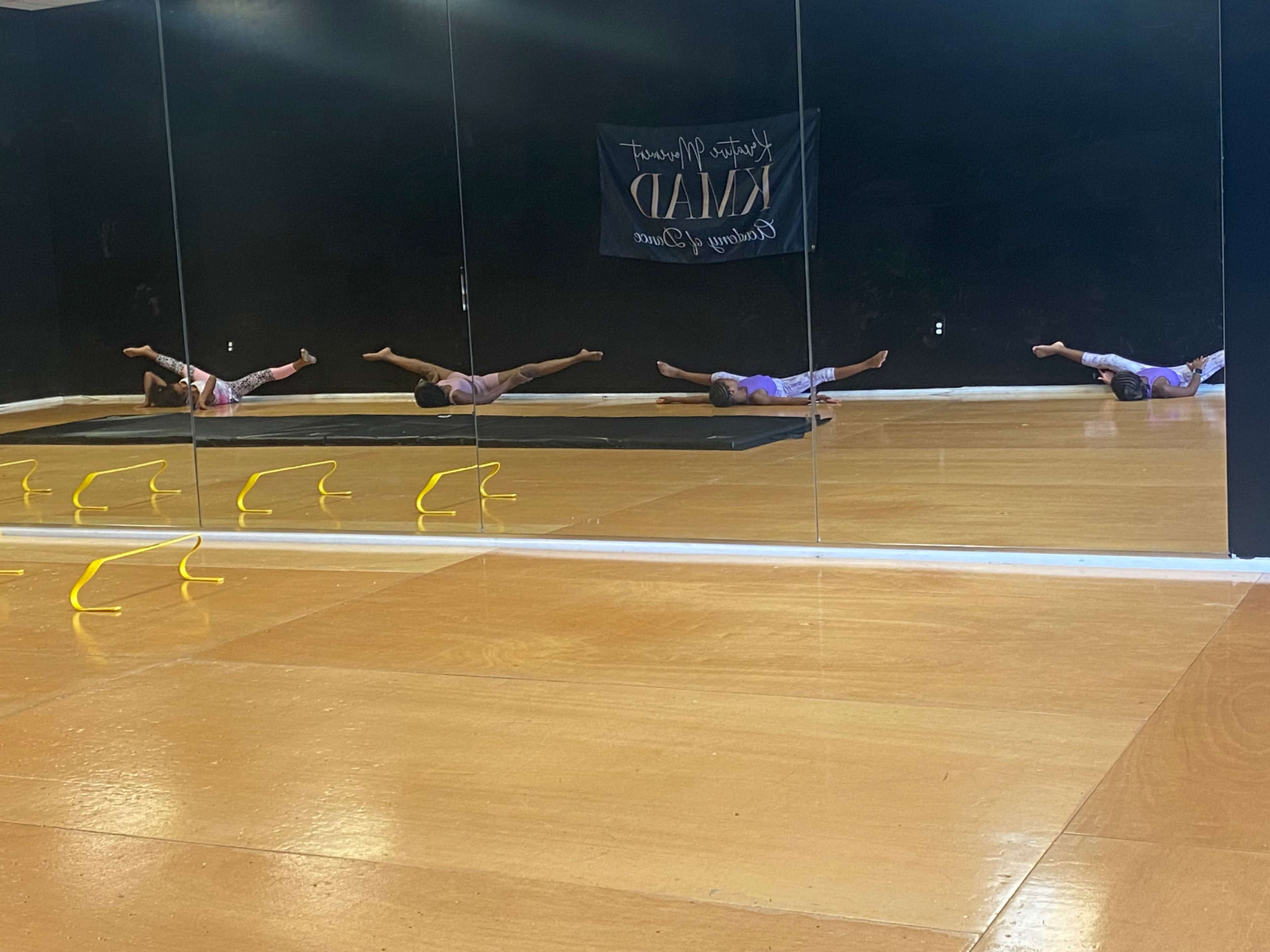 A person performs exercises on a mat in a mirrored room, with yellow agility hurdles positioned in front.