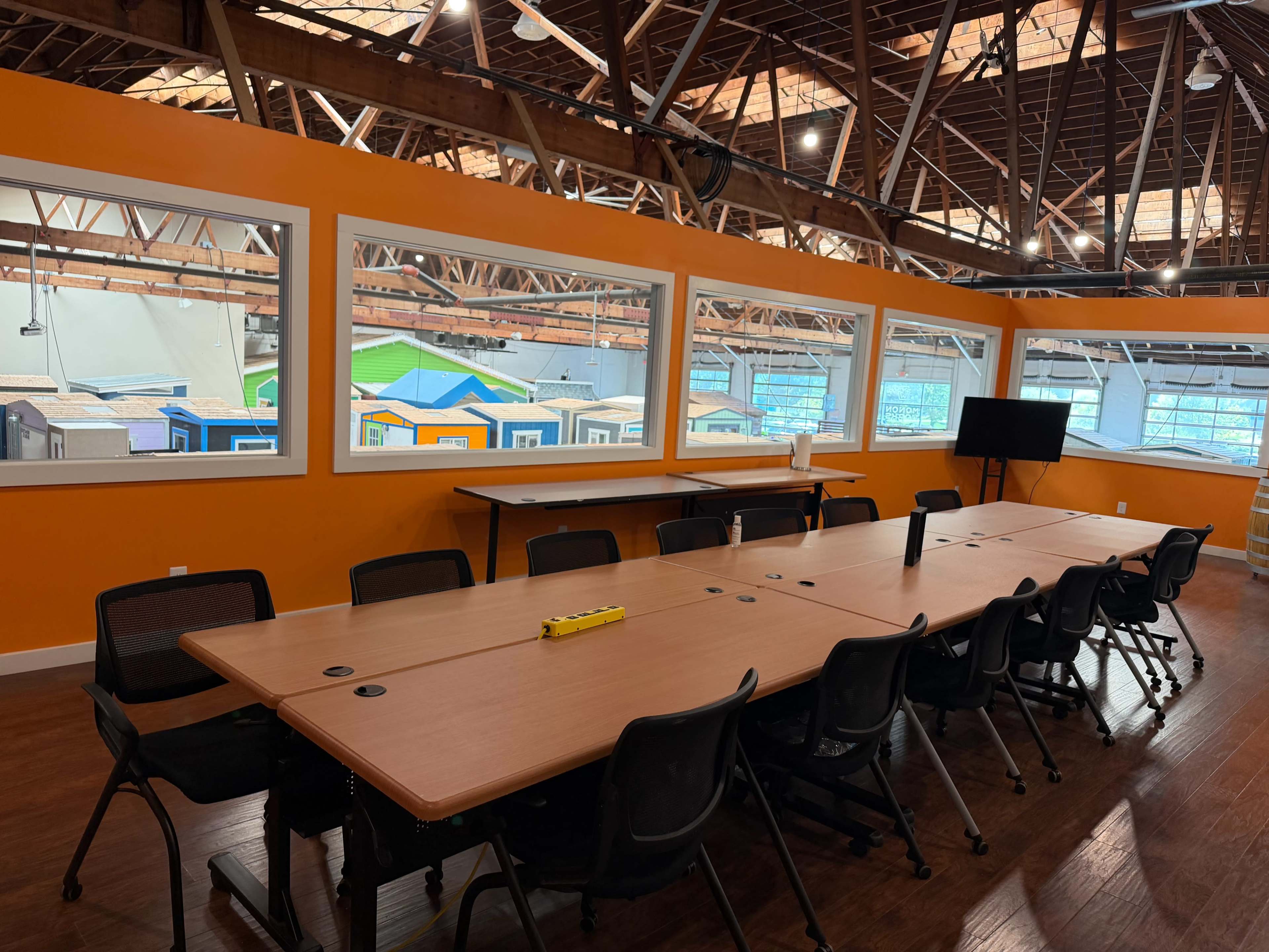 A spacious conference room with a large table, black chairs, and large windows displaying colorful structures outside.