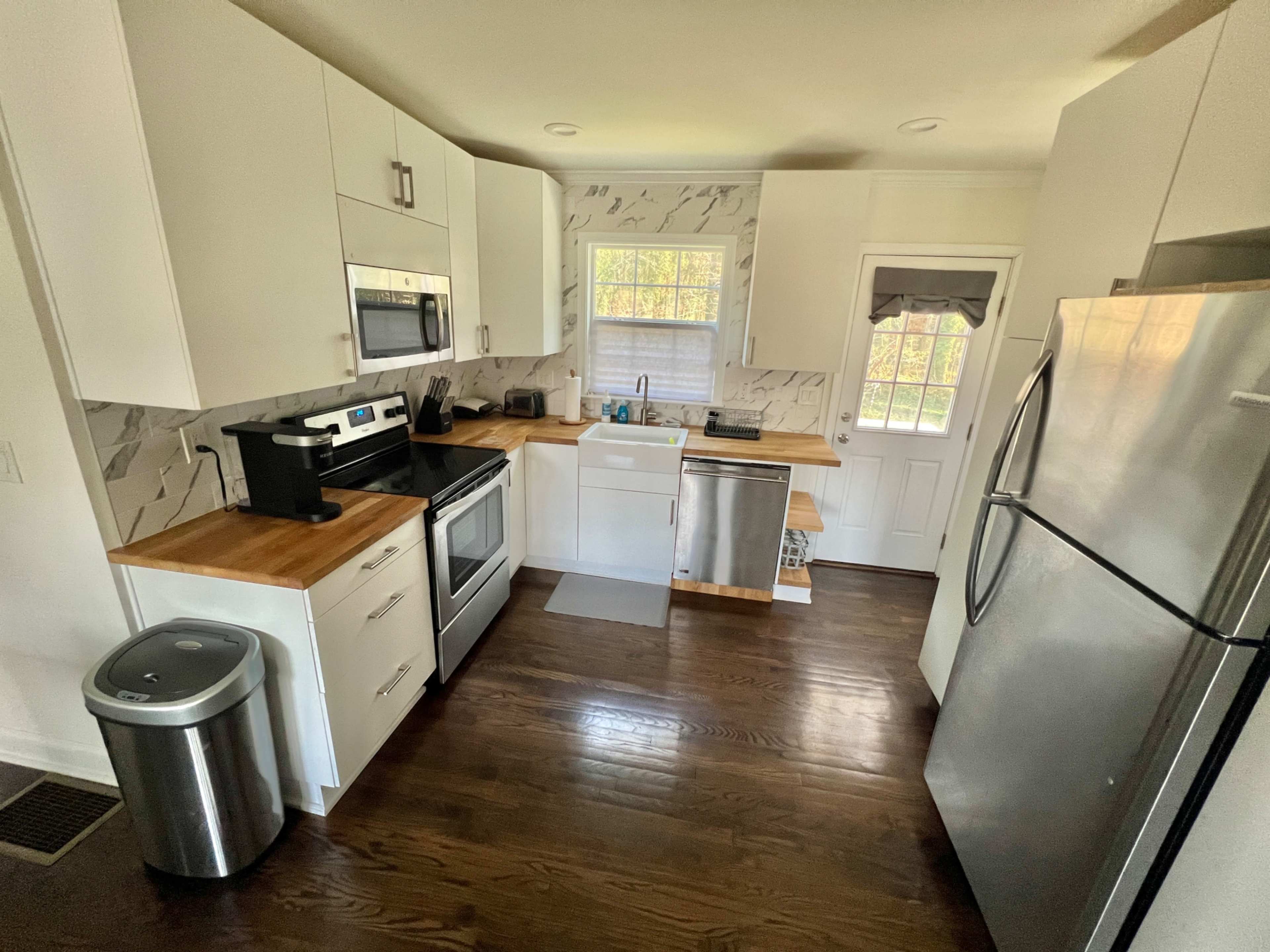 A modern kitchen with white cabinetry, stainless steel appliances, a wooden countertop, and a doorway leading outside.