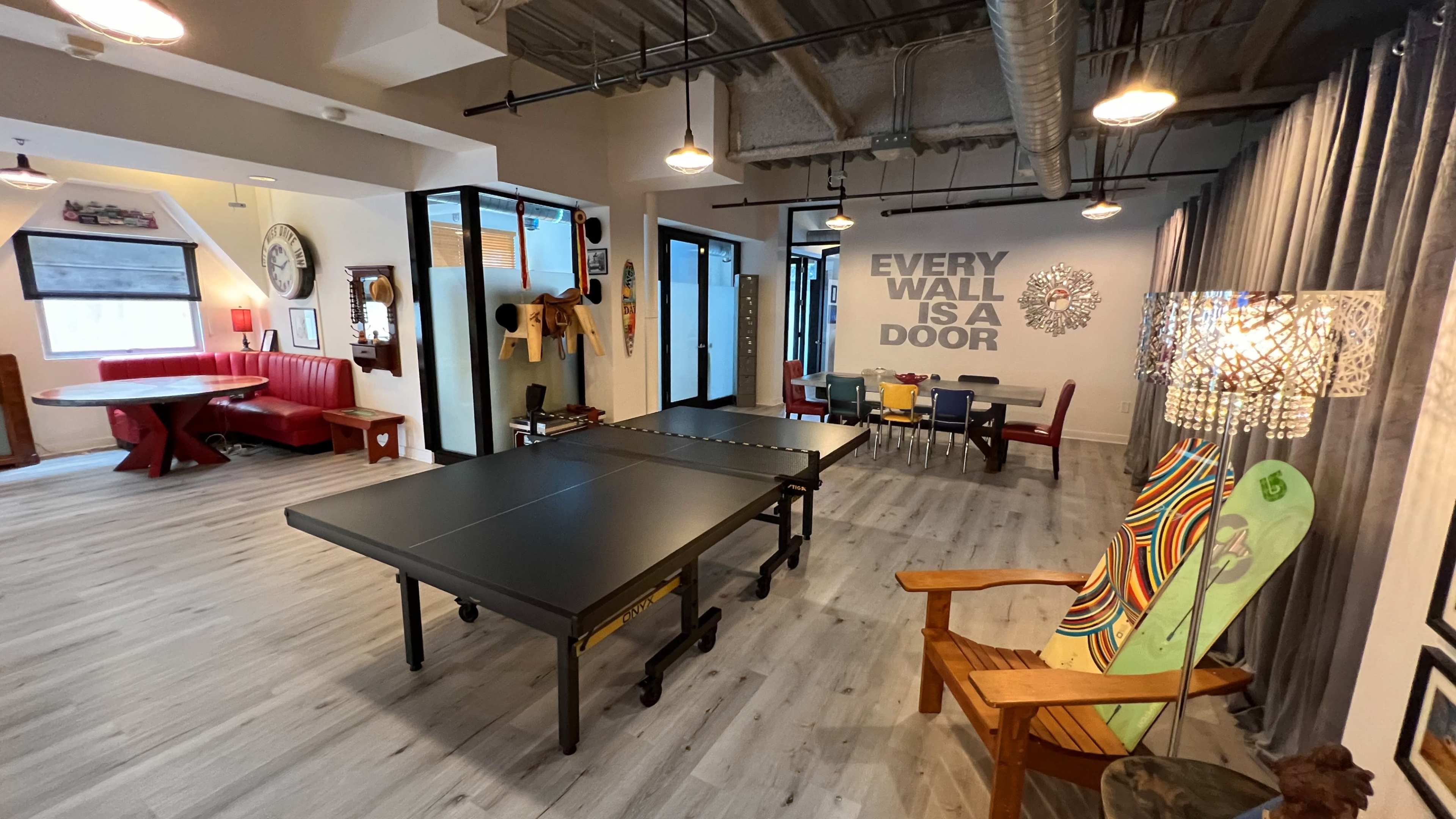 The image shows a spacious room with a table tennis setup, seating areas, and a wall featuring the phrase "EVERY WALL IS A DOOR."