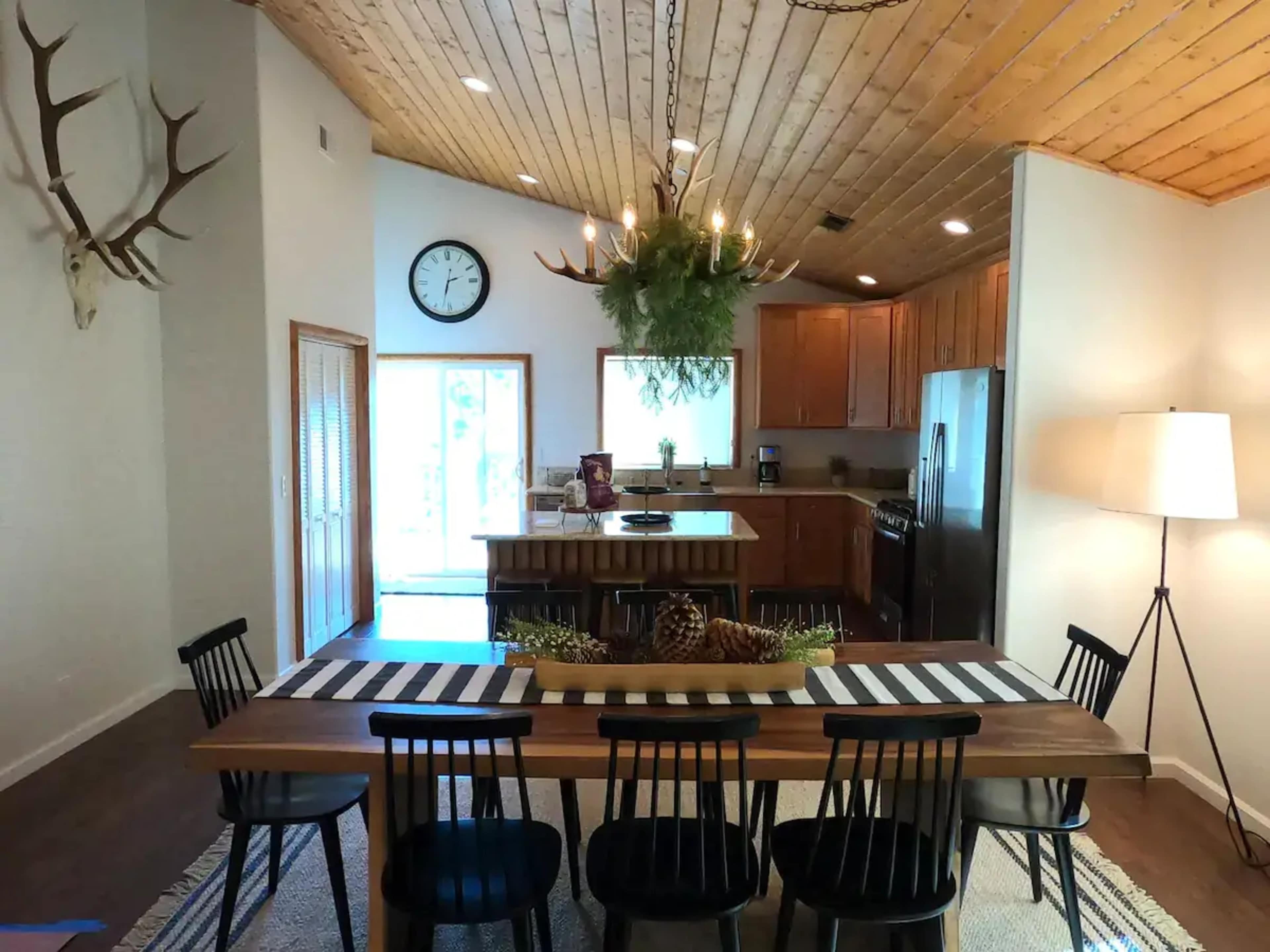 A modern kitchen and dining area features a wooden table with black chairs, a large island, and rustic decor, along with a sliding door leading to an outdoor space.