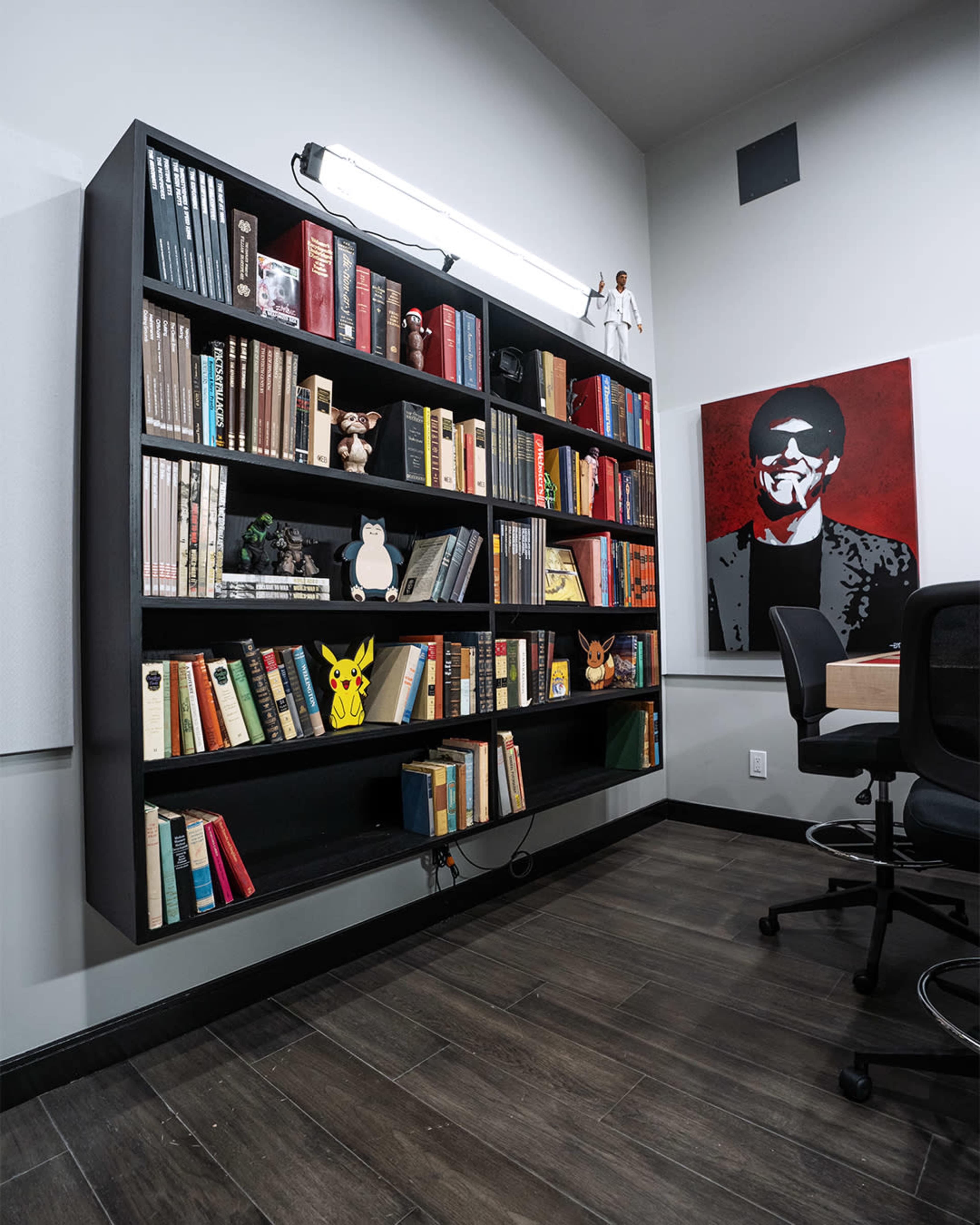 A modern bookshelf filled with various books and collectibles, including figurines and a Pikachu, is mounted against a gray wall.