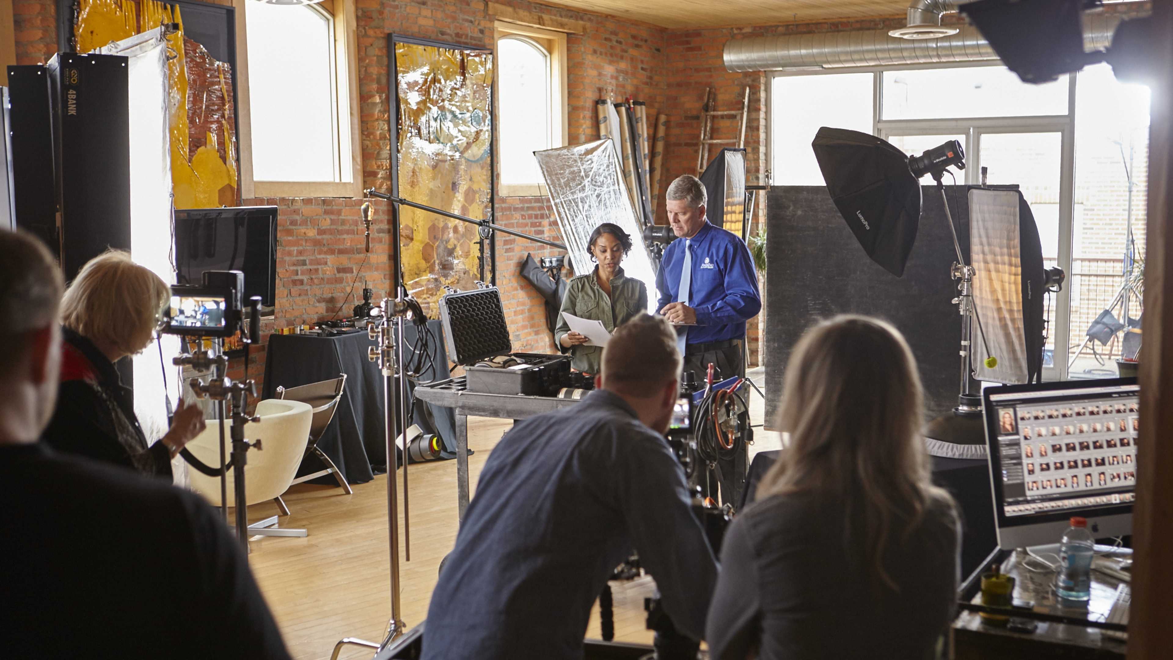 A group of people works in a photography studio, setting up equipment and reviewing shots on a computer.