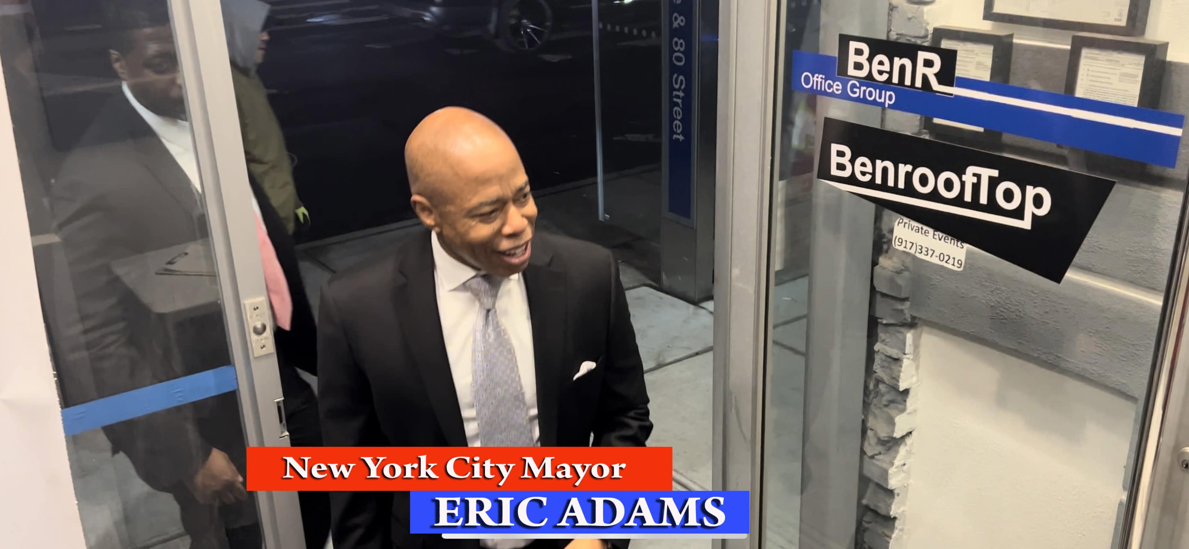 A man in a suit stands at the entrance of a building with signs for BenR Office Group and BenroofTop.