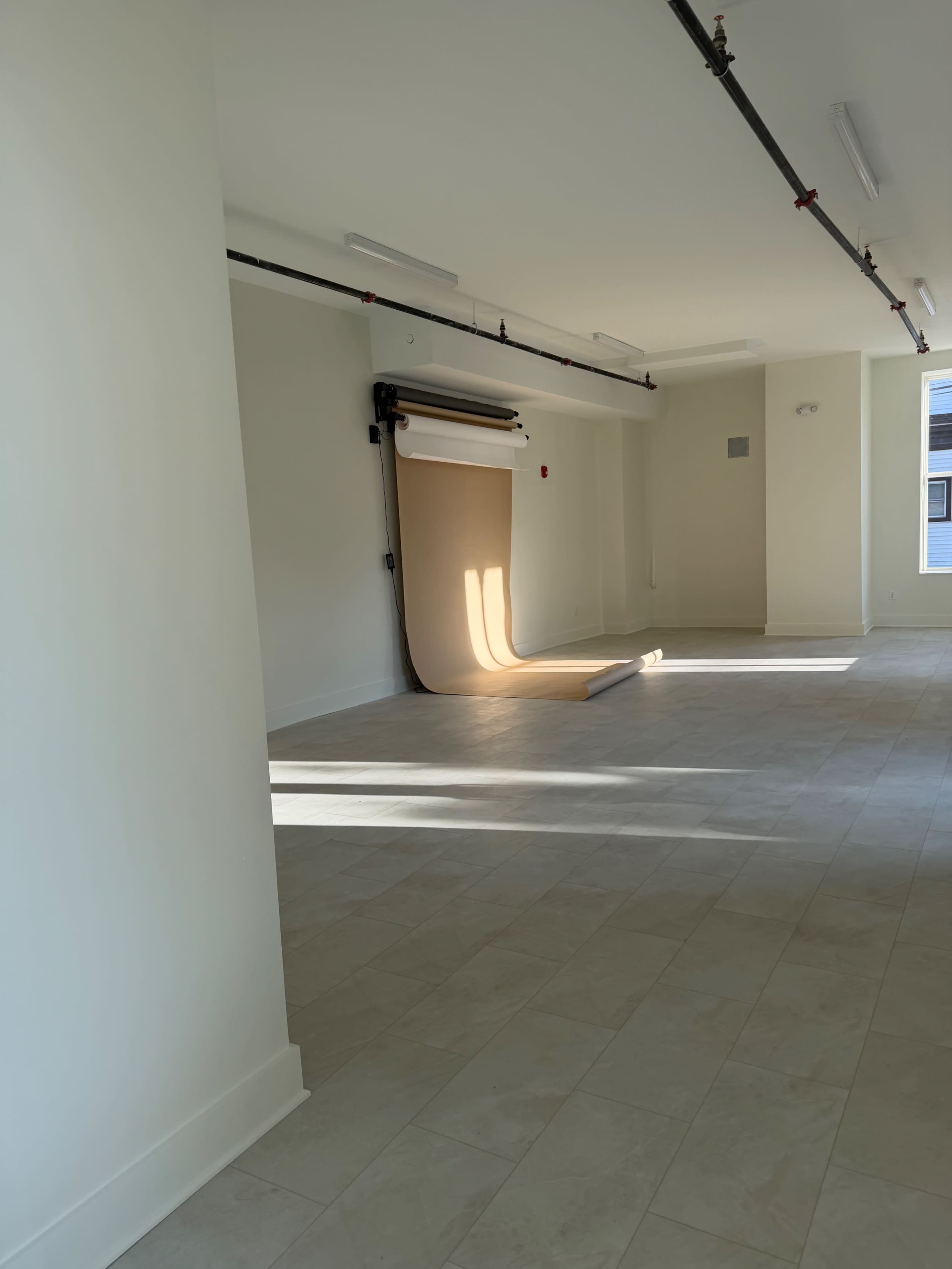 The image shows a spacious, well-lit room with a seamless backdrop setup and neutral-colored walls and flooring.
