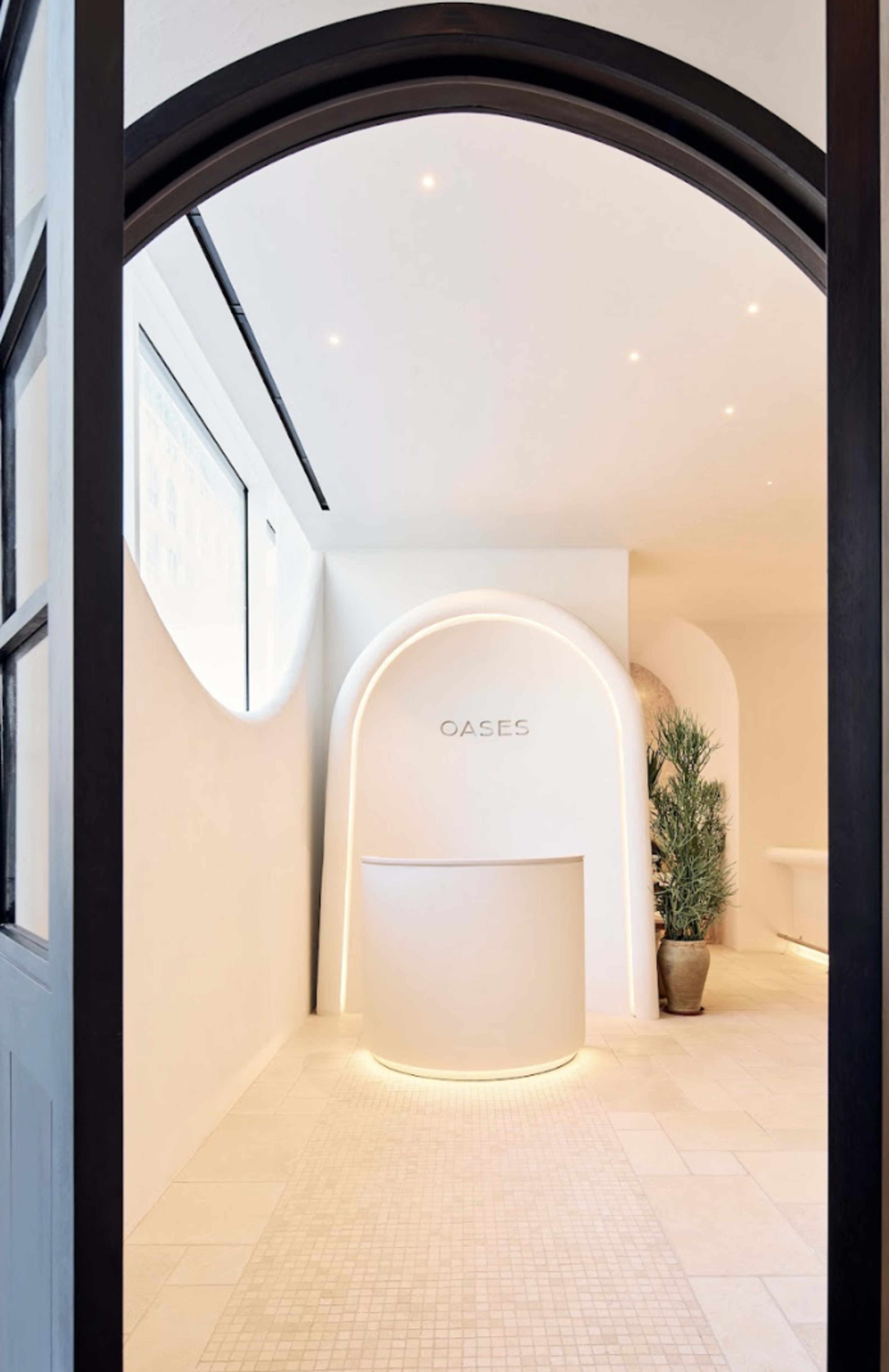 The image shows a modern reception area with a rounded desk and minimalist design, featuring soft lighting and a neutral color palette.