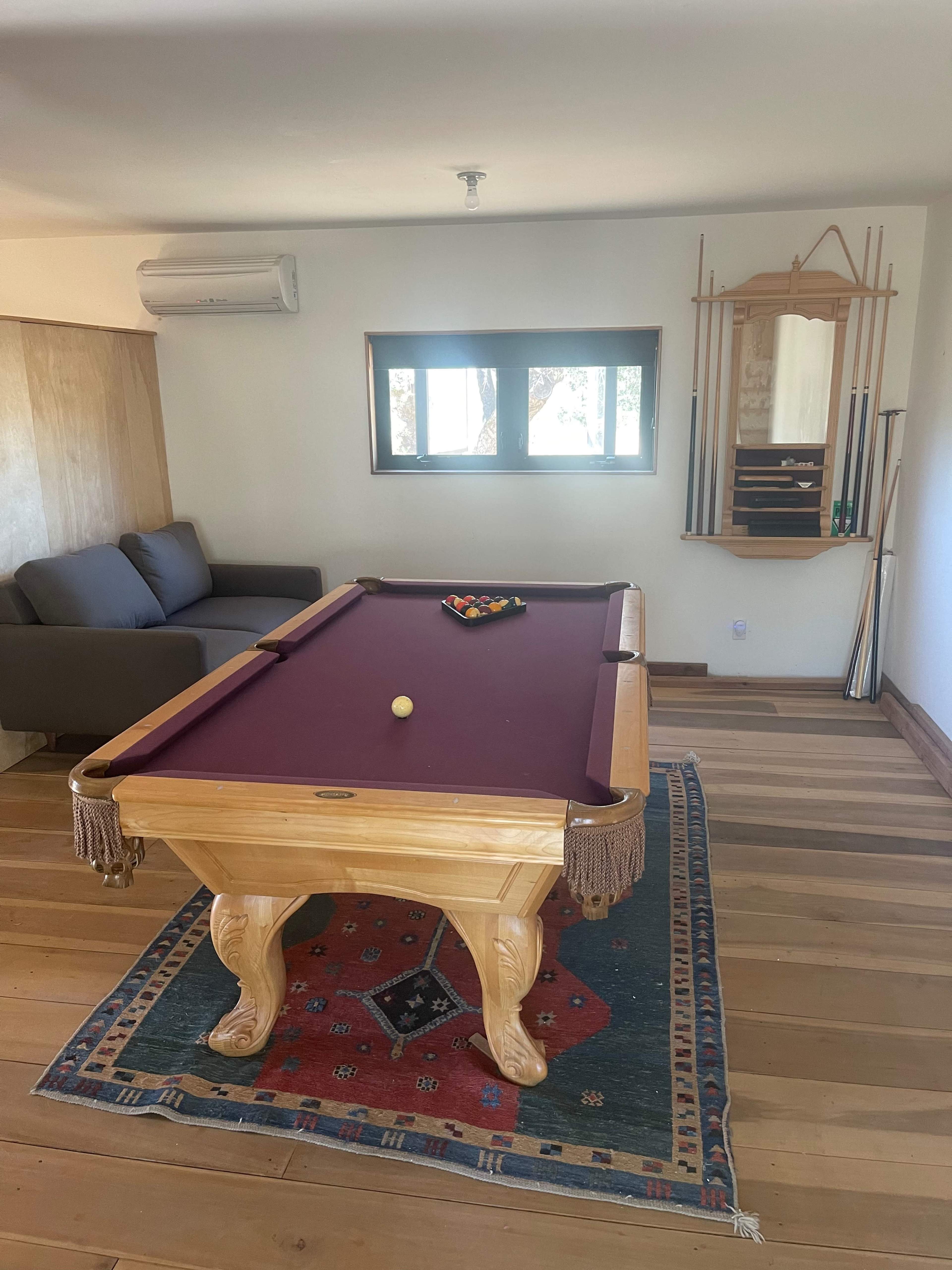 A billiard table with a cue ball and several colored balls arranged on it, set in a room with a sofa and a wooden wall.