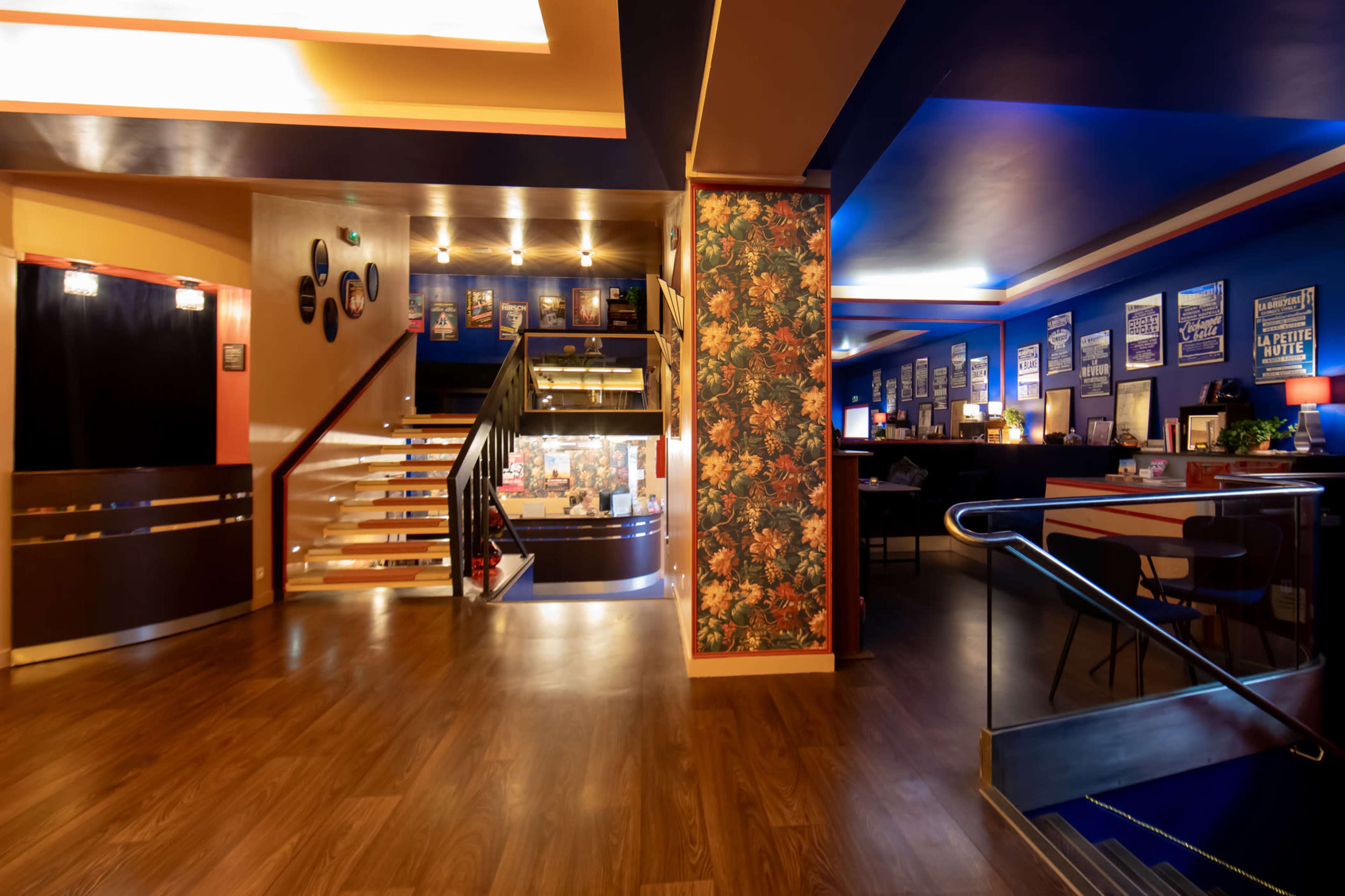 The interior of a brightly lit restaurant or café featuring a mix of colorful walls, a staircase, and various framed posters.