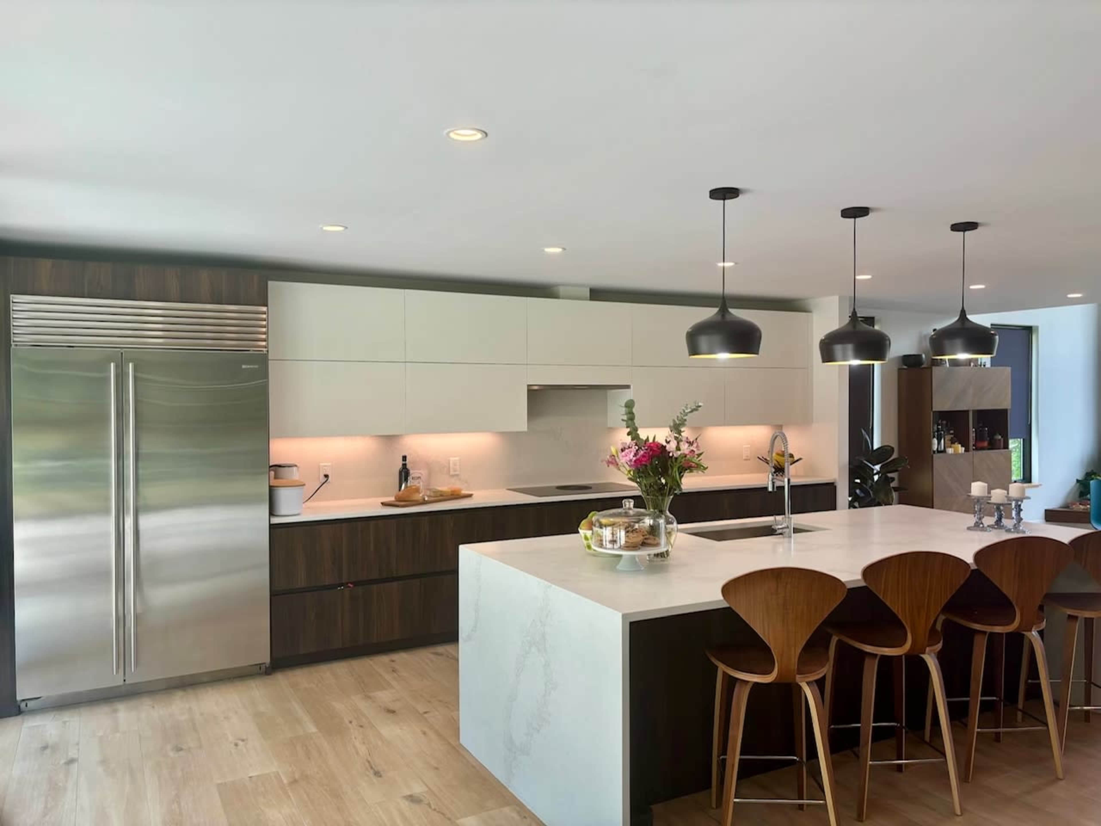 A modern kitchen featuring a stainless steel refrigerator, a large island with a marble countertop, and wooden bar stools.