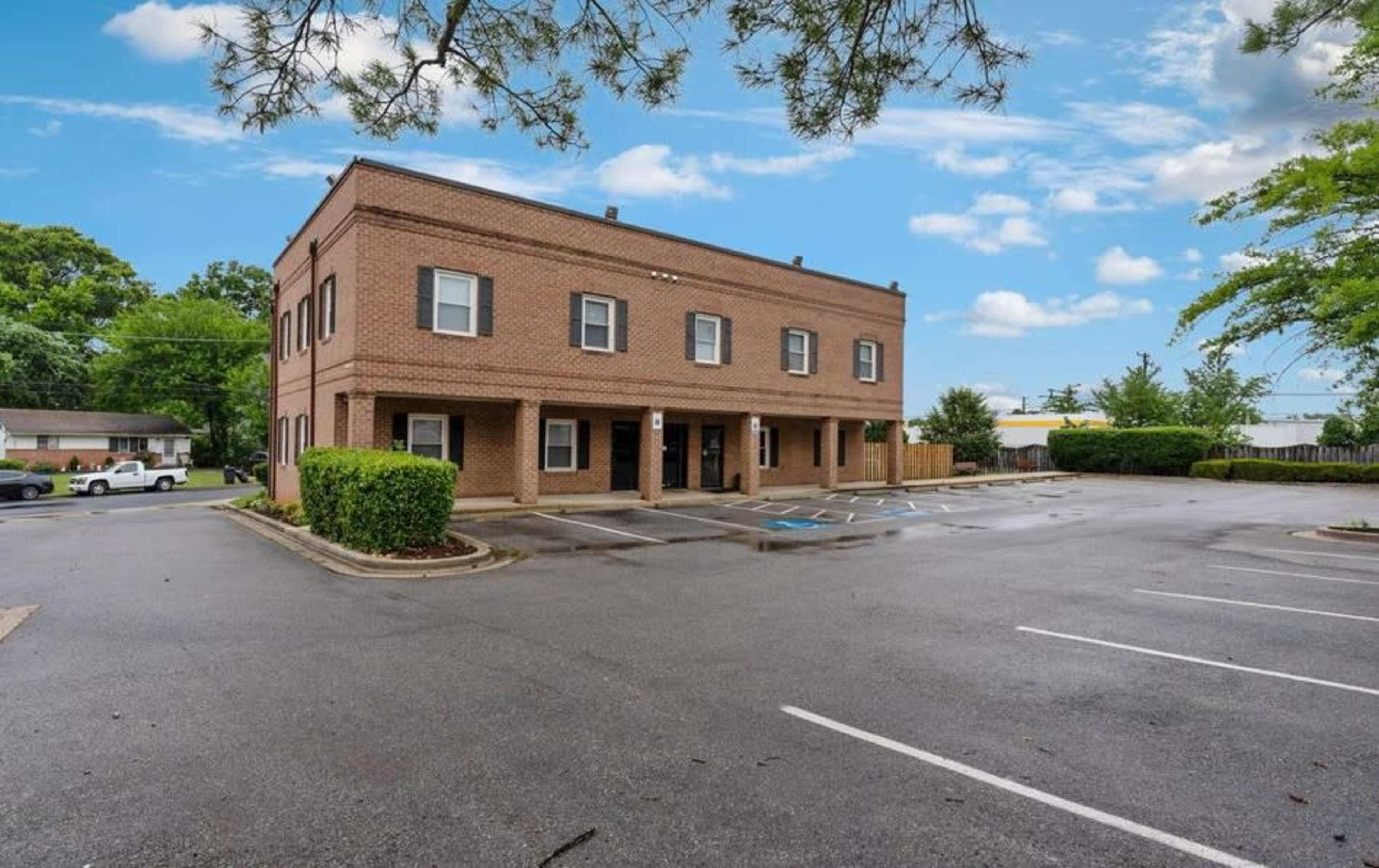 A two-story brick building with several parking spaces in front of it is surrounded by grass and trees.