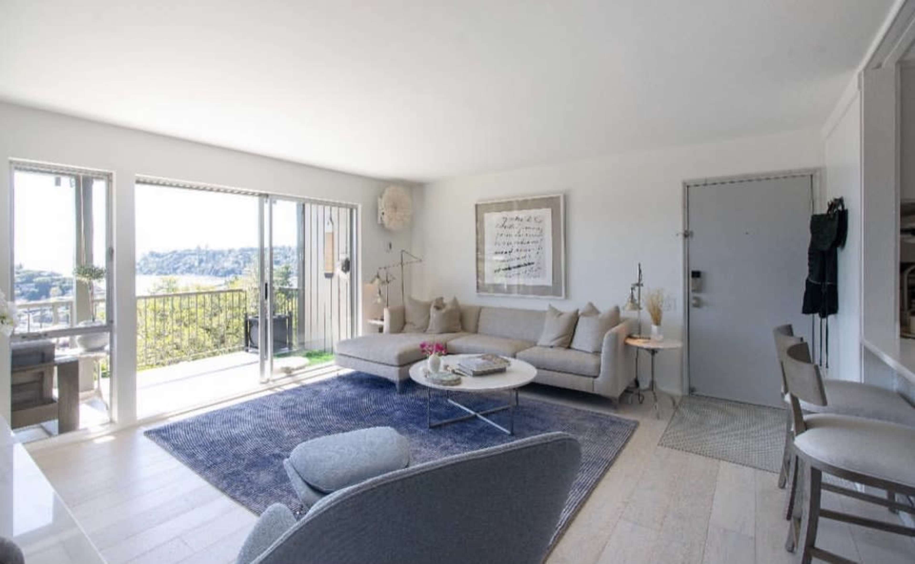 A bright, modern living room featuring a sectional sofa, a coffee table, and large windows that open to a balcony with a view.