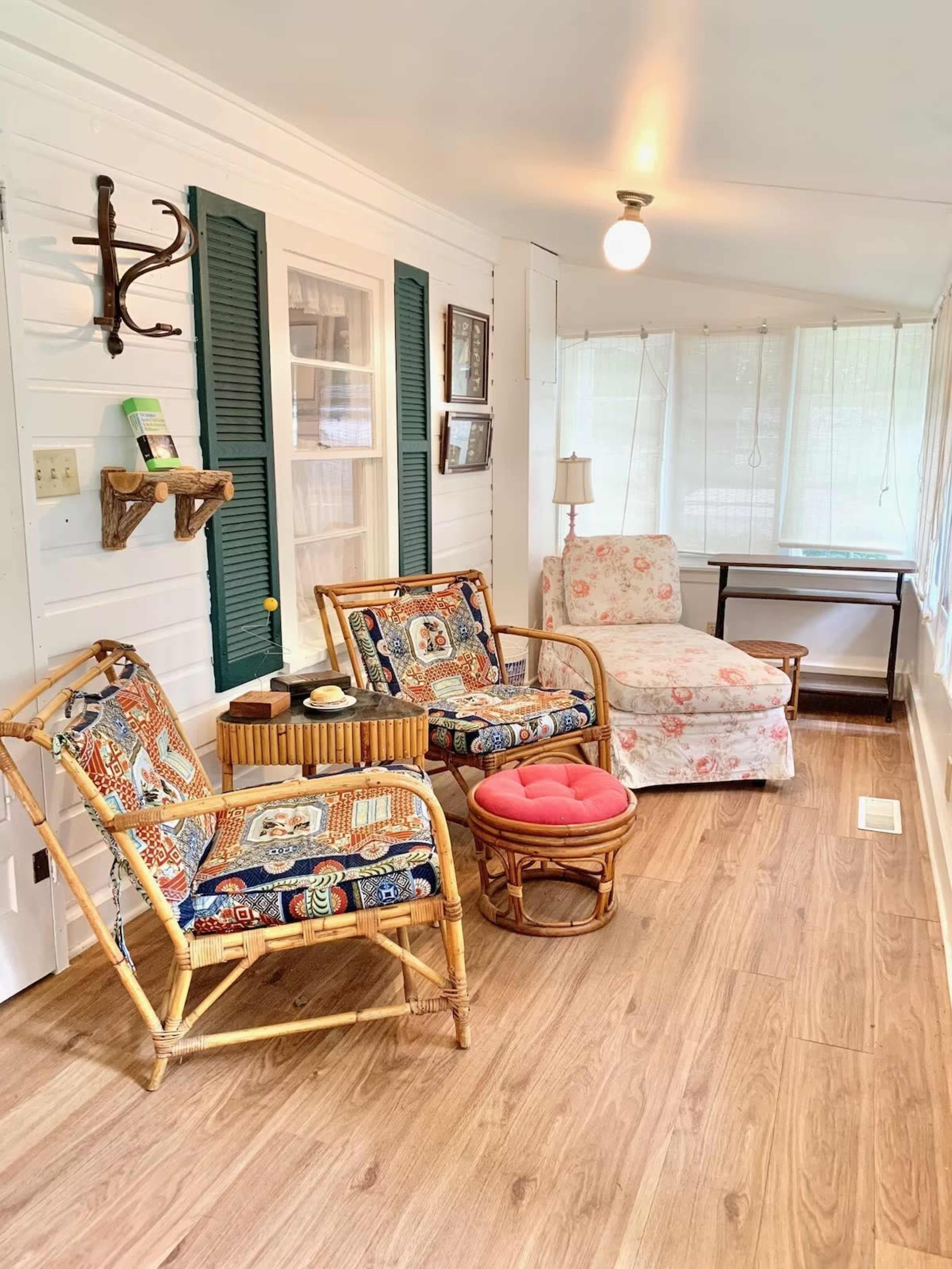 A sunroom with two rattan chairs, a floral armchair, a small table, and large windows allowing natural light to enter.