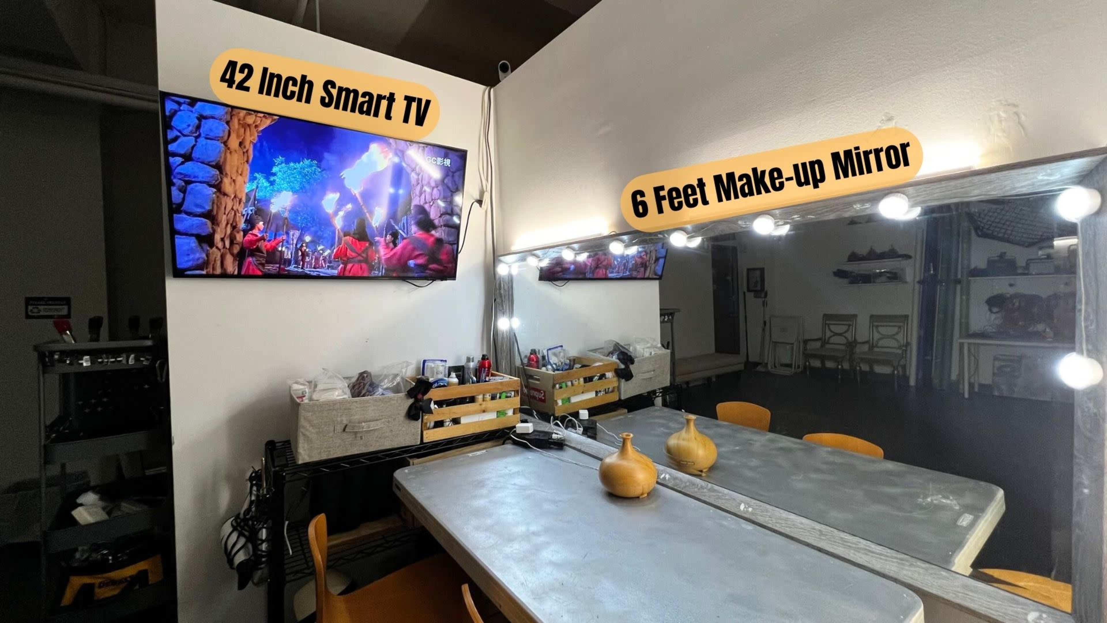 The image shows a room with a 42-inch smart TV mounted on the wall and a six-foot make-up mirror with illuminated lights above a table.