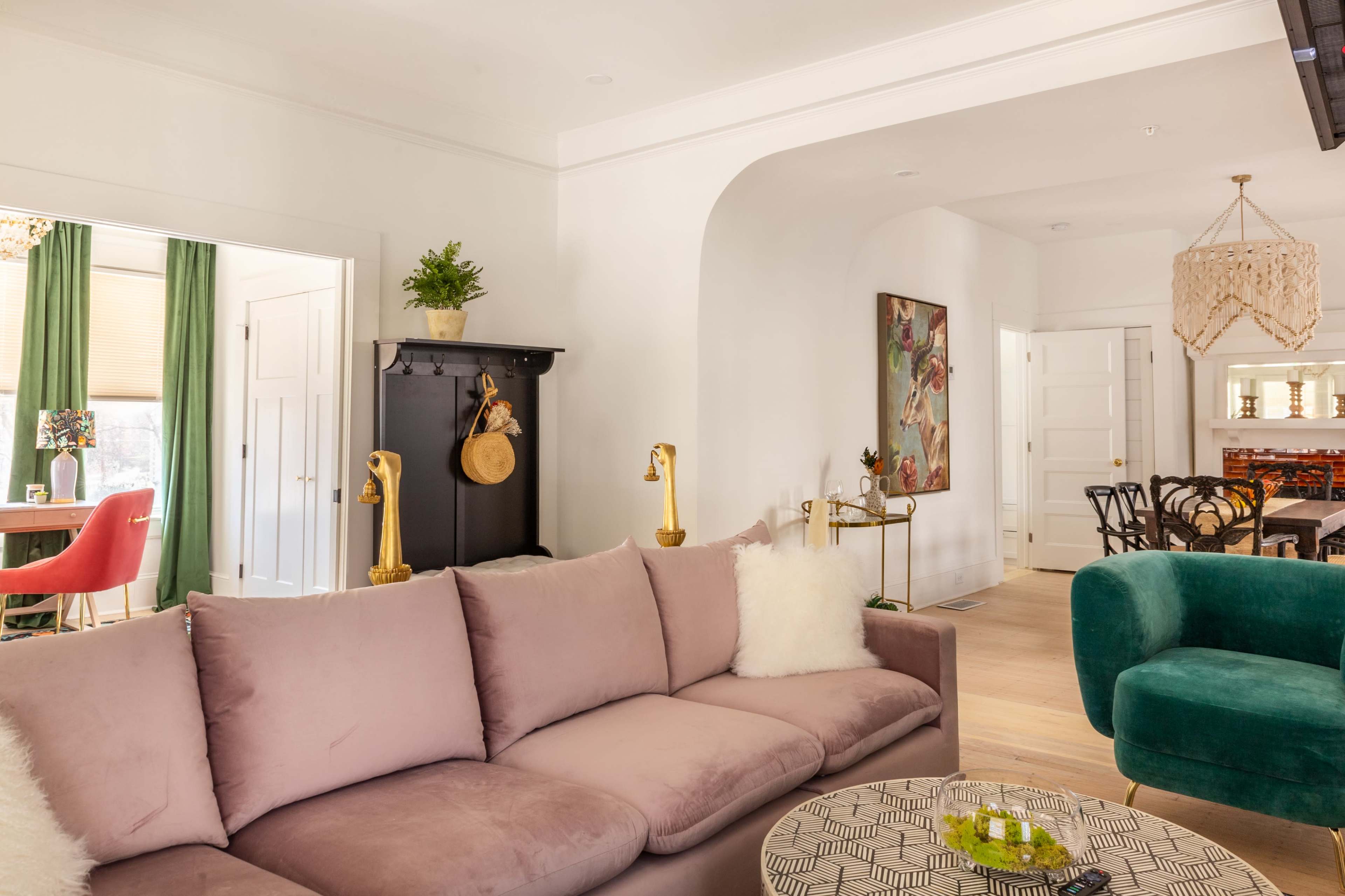 A living room with a pink sofa, a green accent chair, and an arched entryway leading to other rooms.