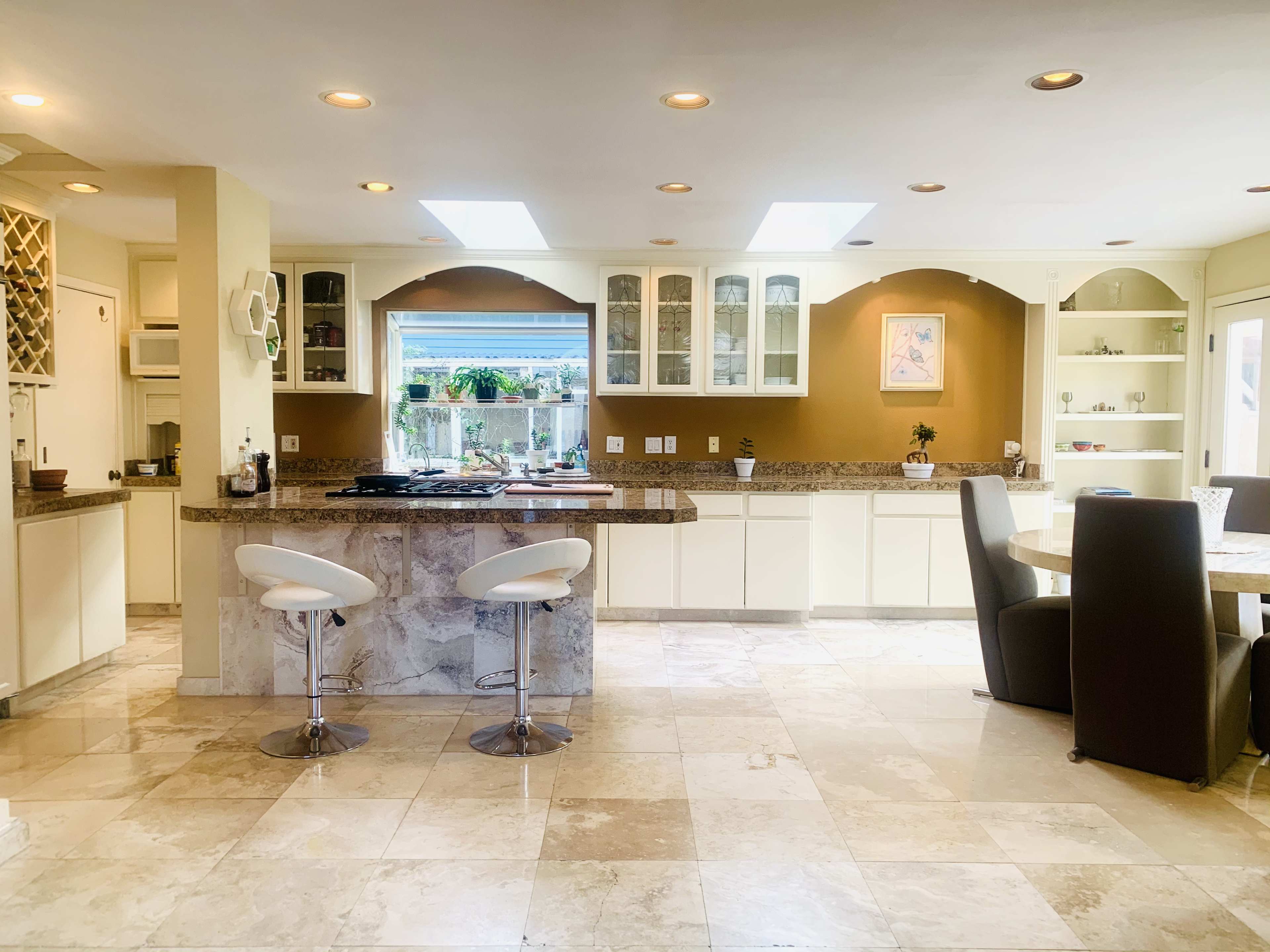 A modern kitchen and dining area with marble floors, a central island with bar stools, and ample cabinetry along the walls.