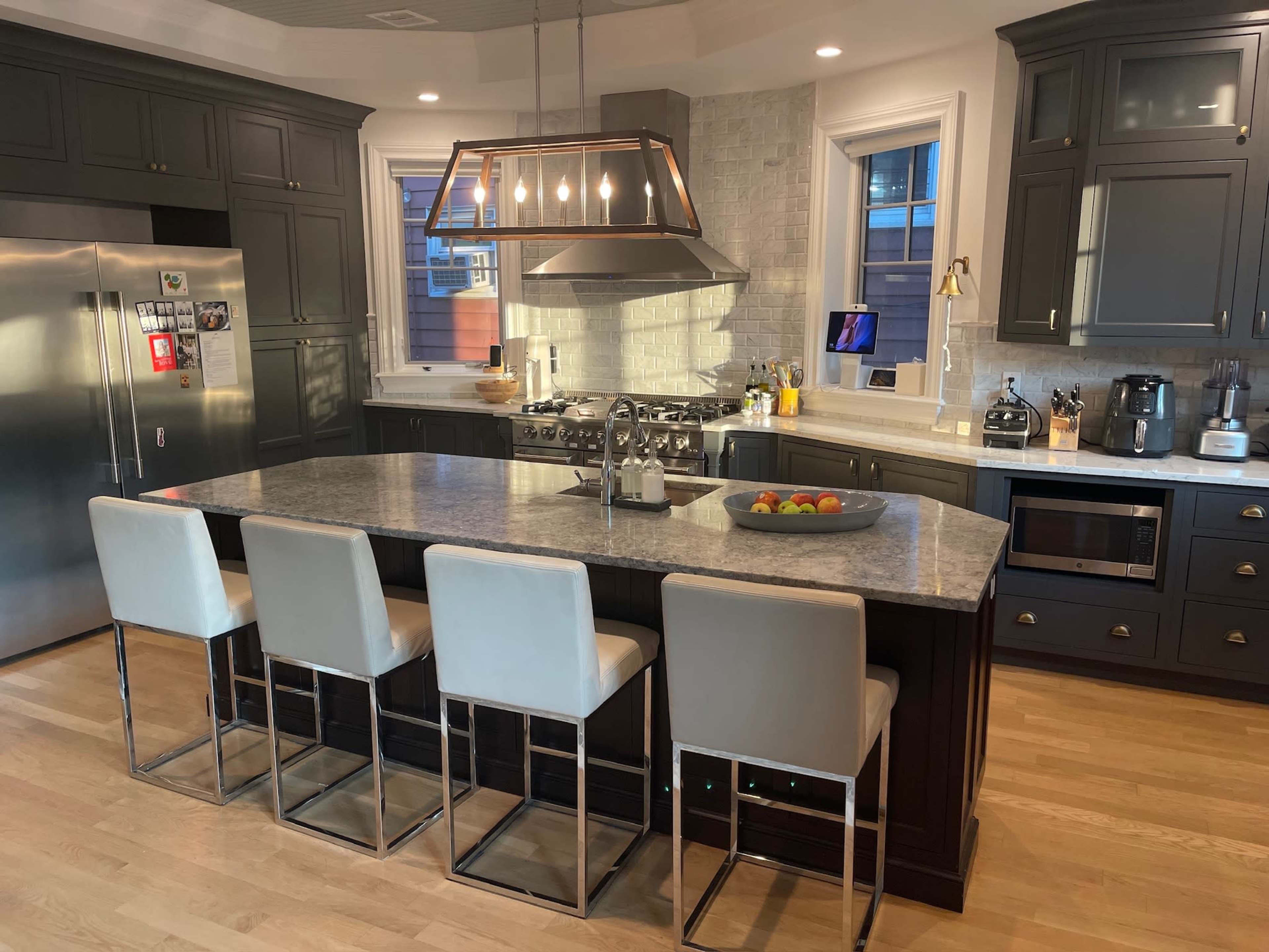The image shows a modern kitchen featuring a large island with seating, stainless steel appliances, and a mix of dark cabinetry and light countertops.