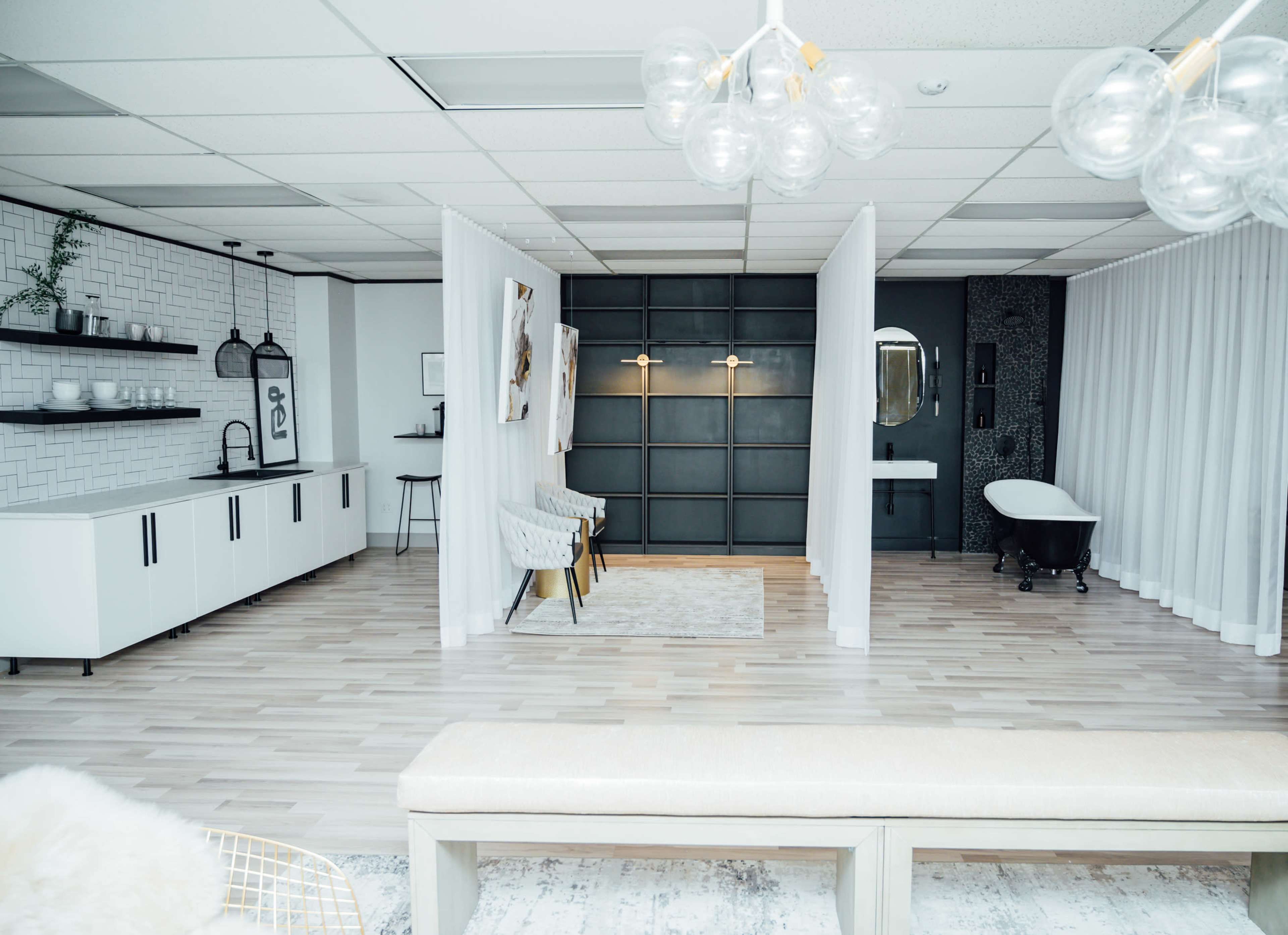 A modern, open space featuring a white and gray color palette, with separated areas defined by curtain partitions and a freestanding bathtub in the background.