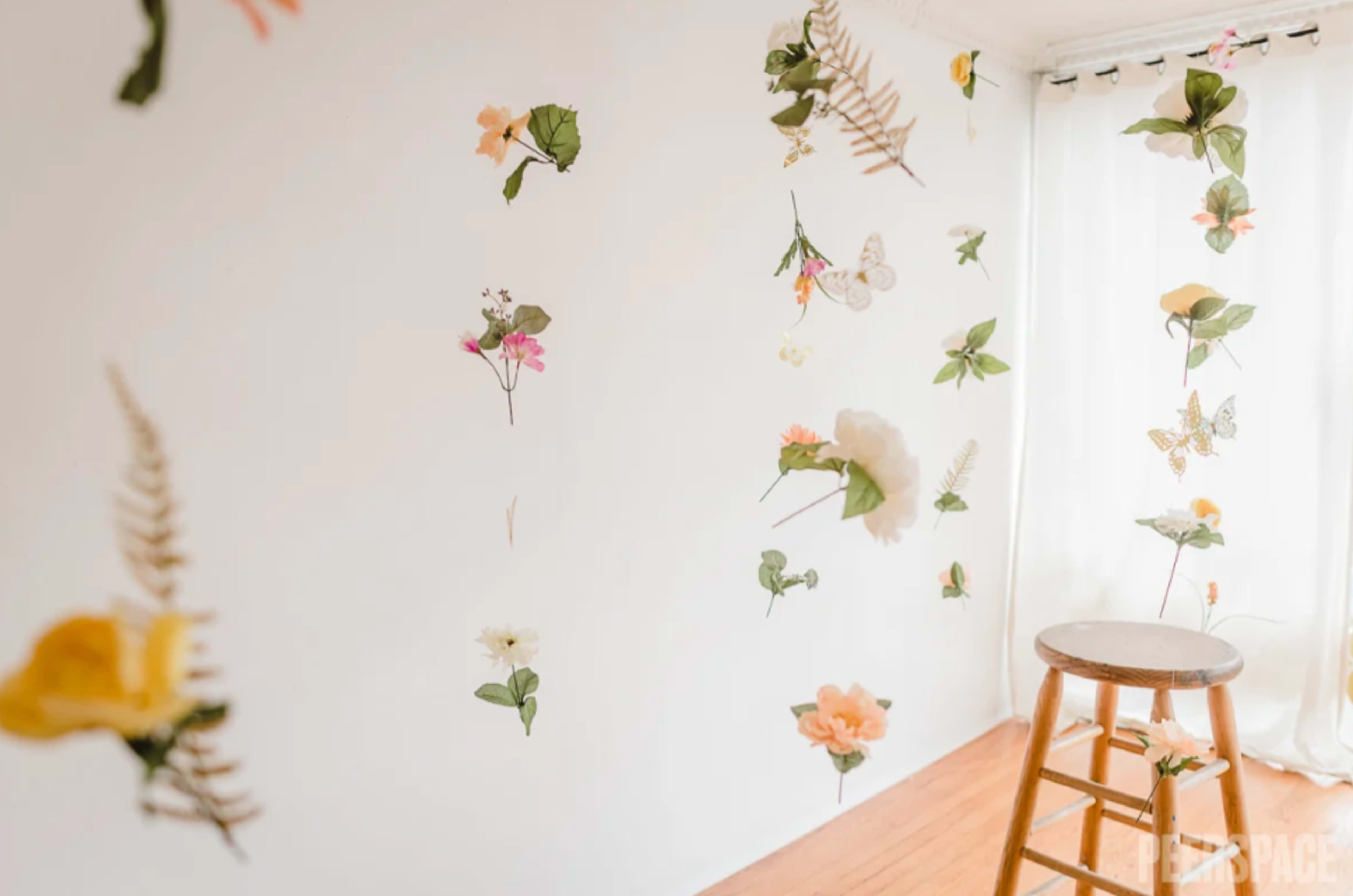 A bright room with a white wall decorated with floral and butterfly designs, while a wooden stool stands on the wooden floor.