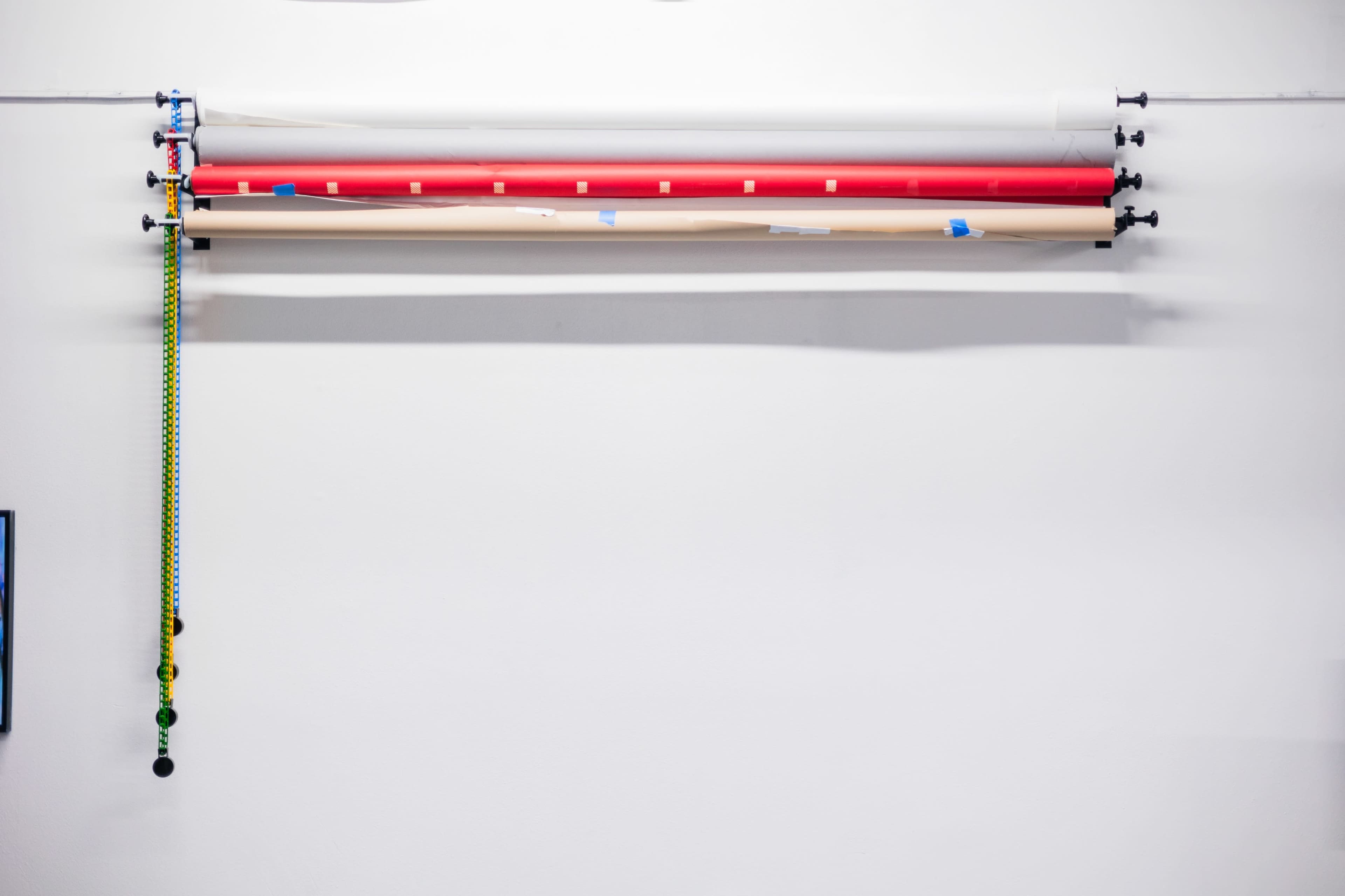 A wall-mounted shelf with several rolls of colorful paper and a green and black strap hanging beside them.