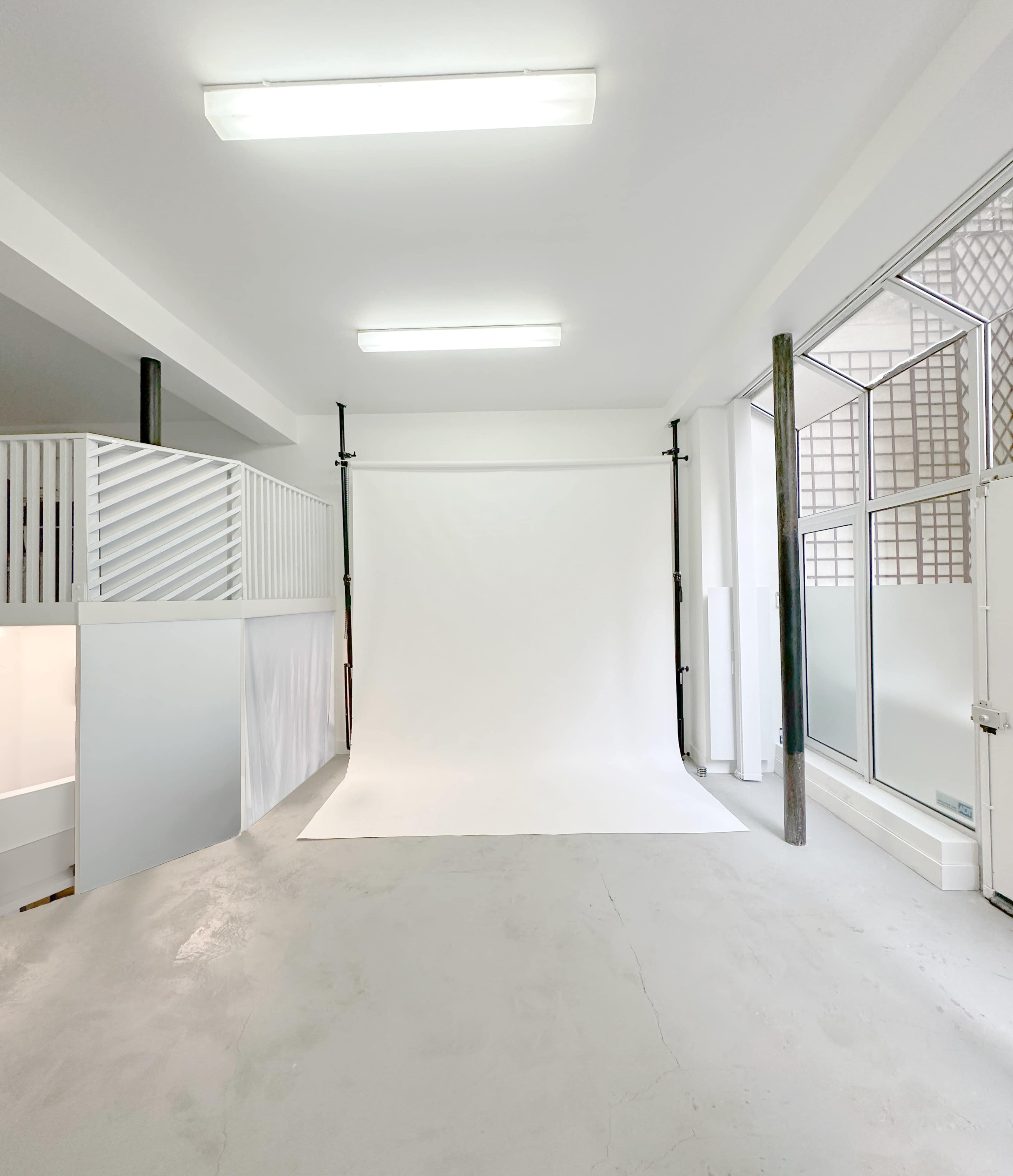 The image shows a well-lit photography studio with a white backdrop and plain gray flooring.