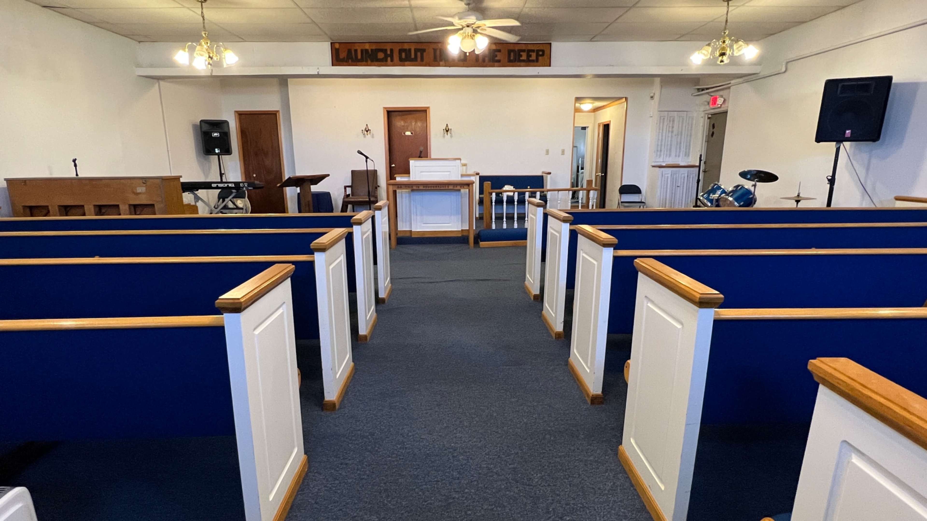 The interior of a church with blue pews facing a white altar and a small stage area.