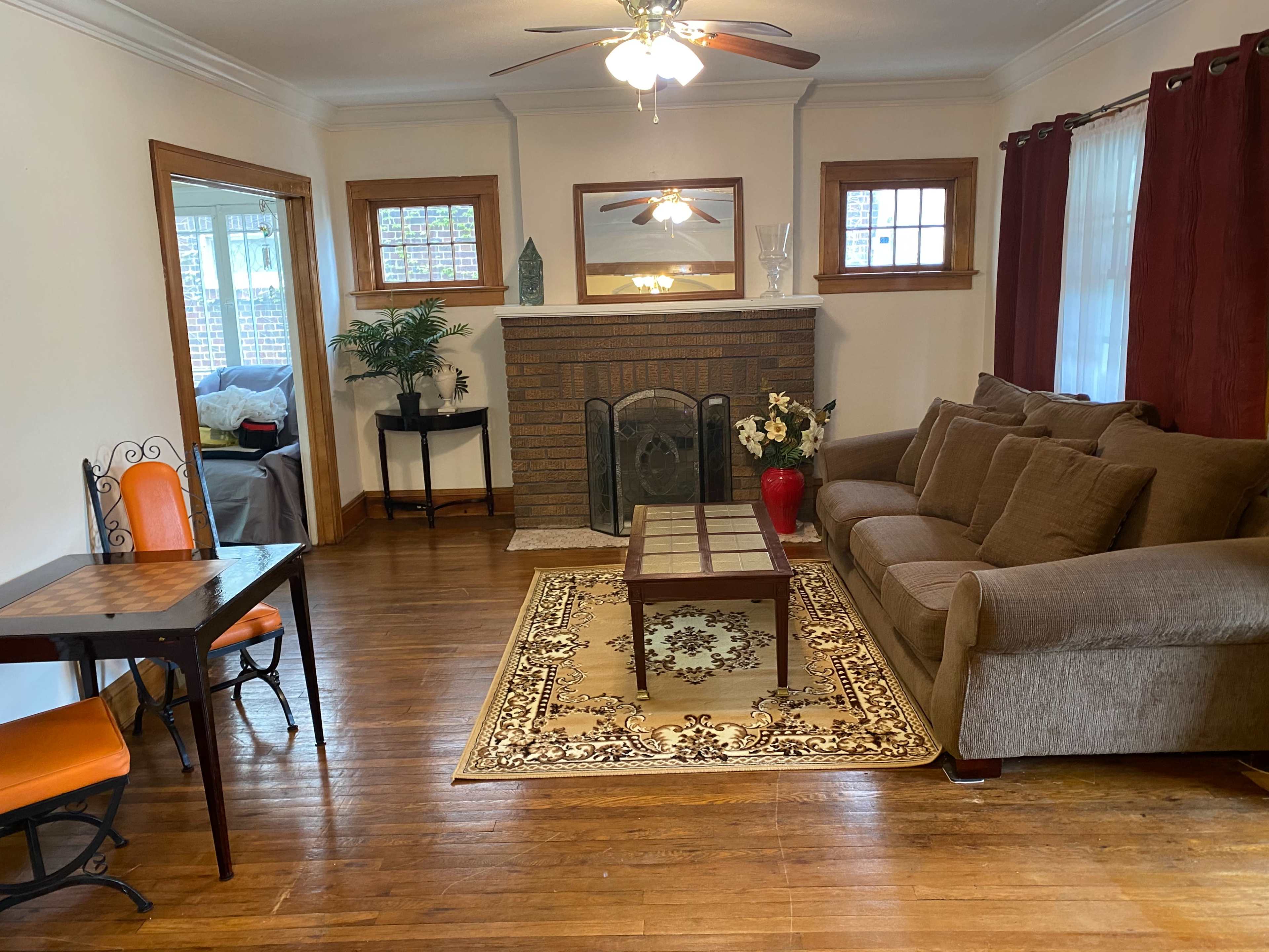 The living room features a brown sofa, a wooden coffee table, a fireplace with a decorative mantel, and a small dining table with orange chairs.
