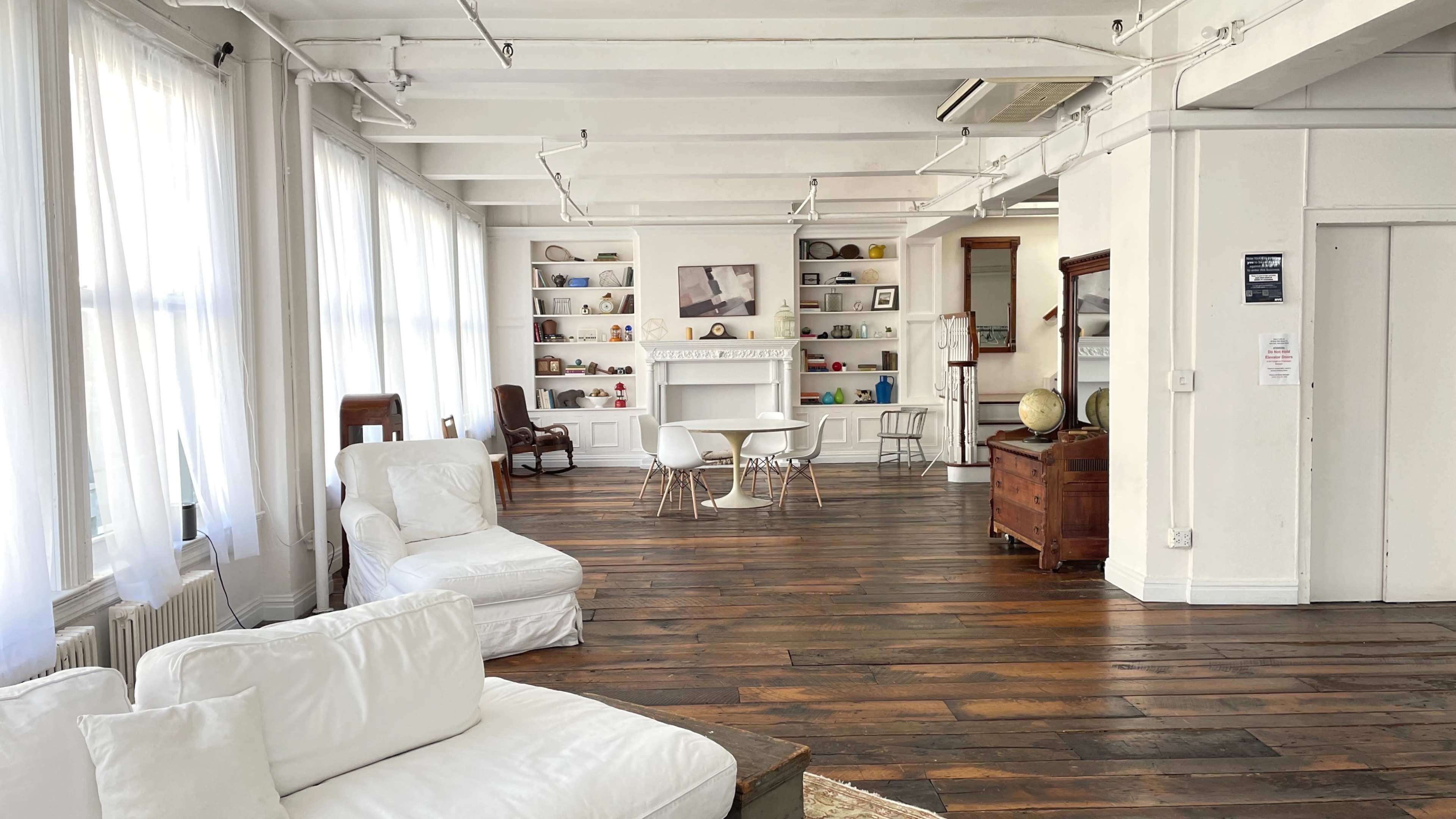 A bright, airy room with wooden floors, white furnishings, and shelves displaying various decorative items.