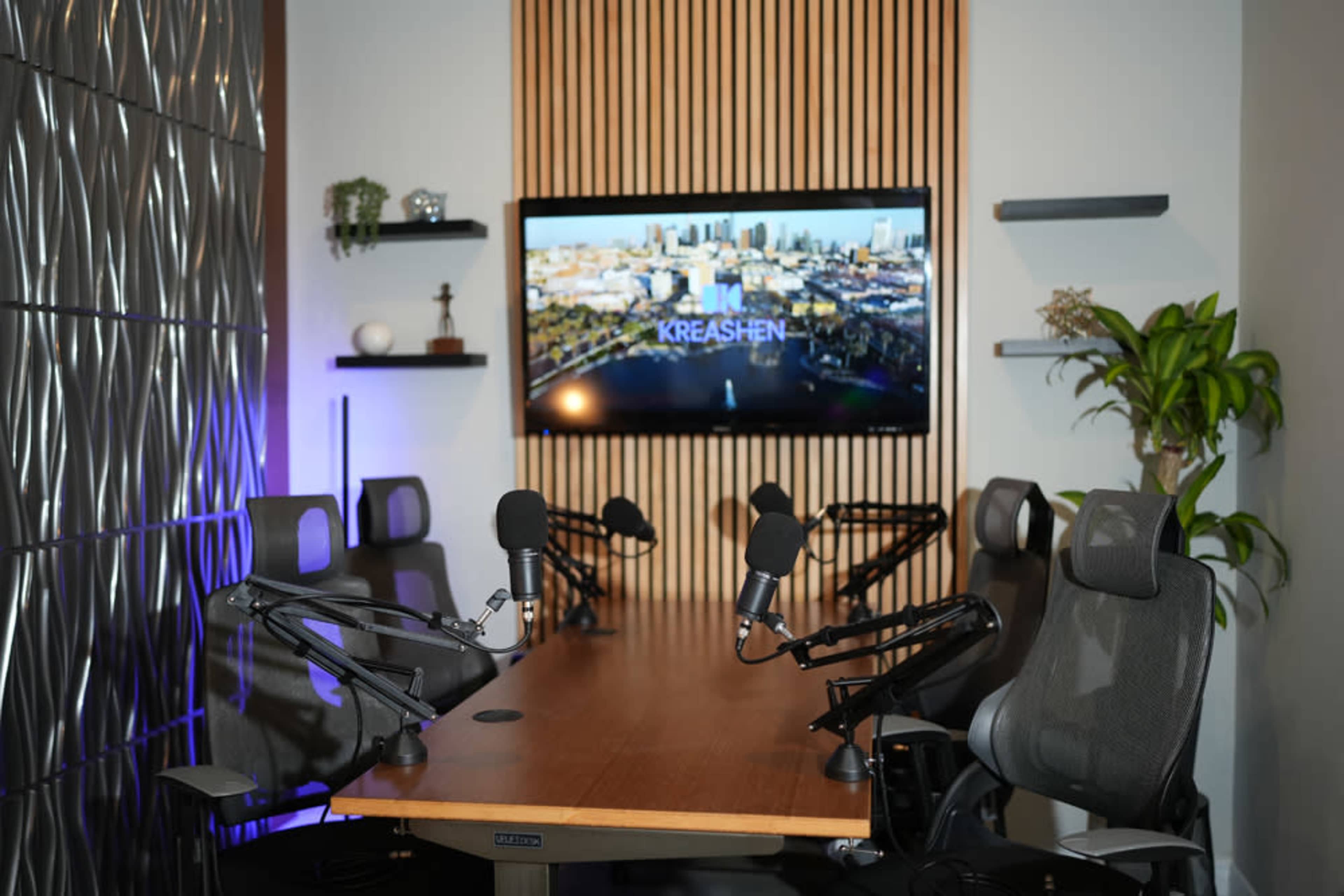 A modern conference room features a wooden table with multiple microphone-equipped chairs and a large screen displaying a cityscape backdrop.