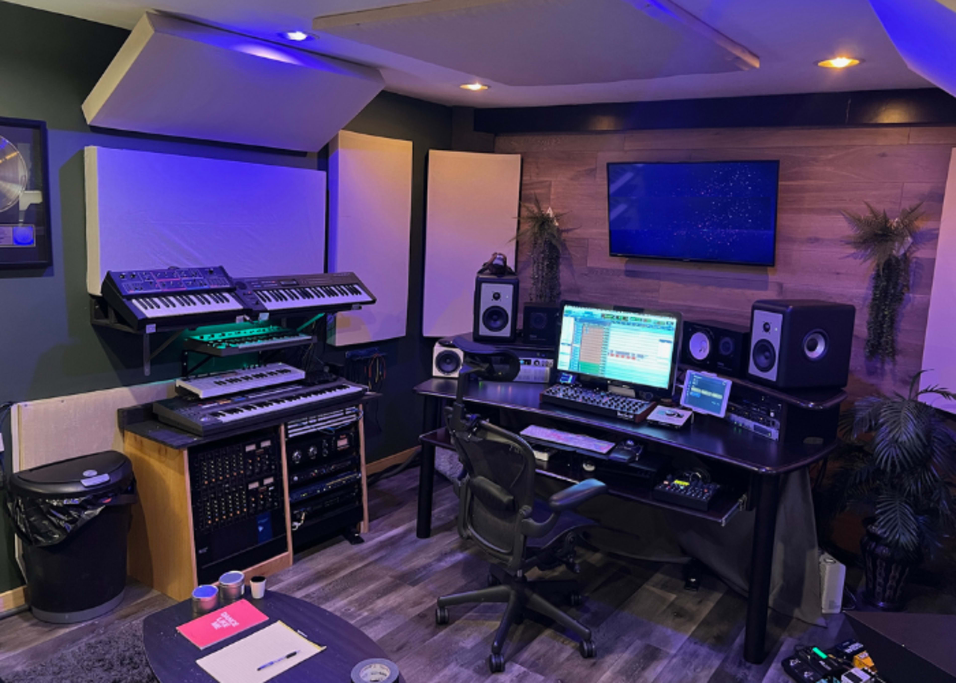 The image shows a music production studio with keyboards, audio equipment, and a computer workstation.