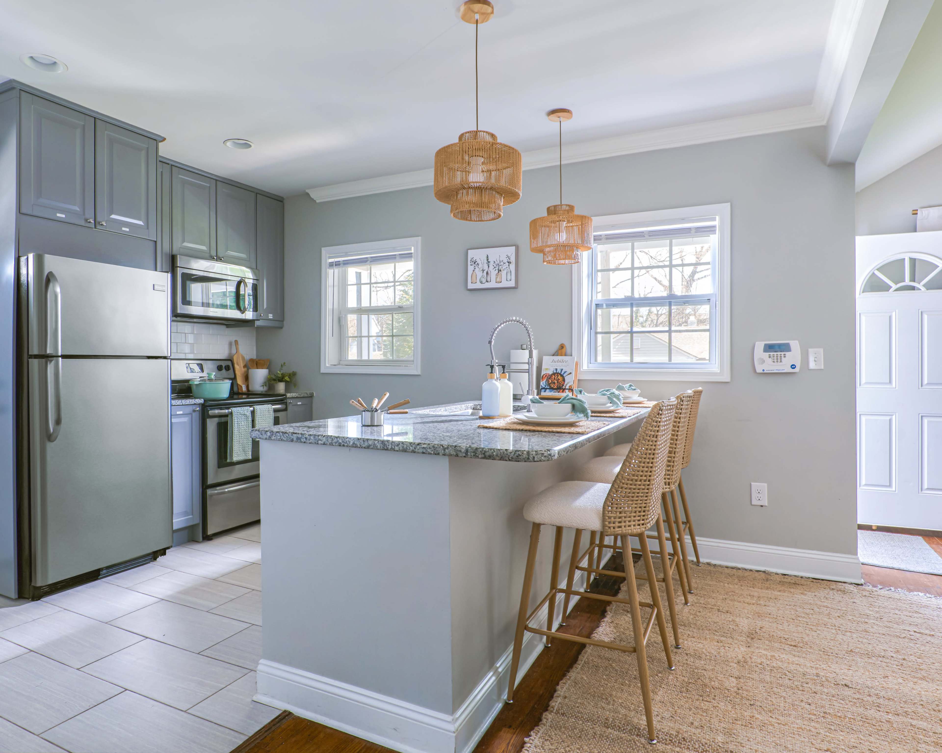 The image shows a modern kitchen with gray cabinetry, stainless steel appliances, and a spacious island with seating.