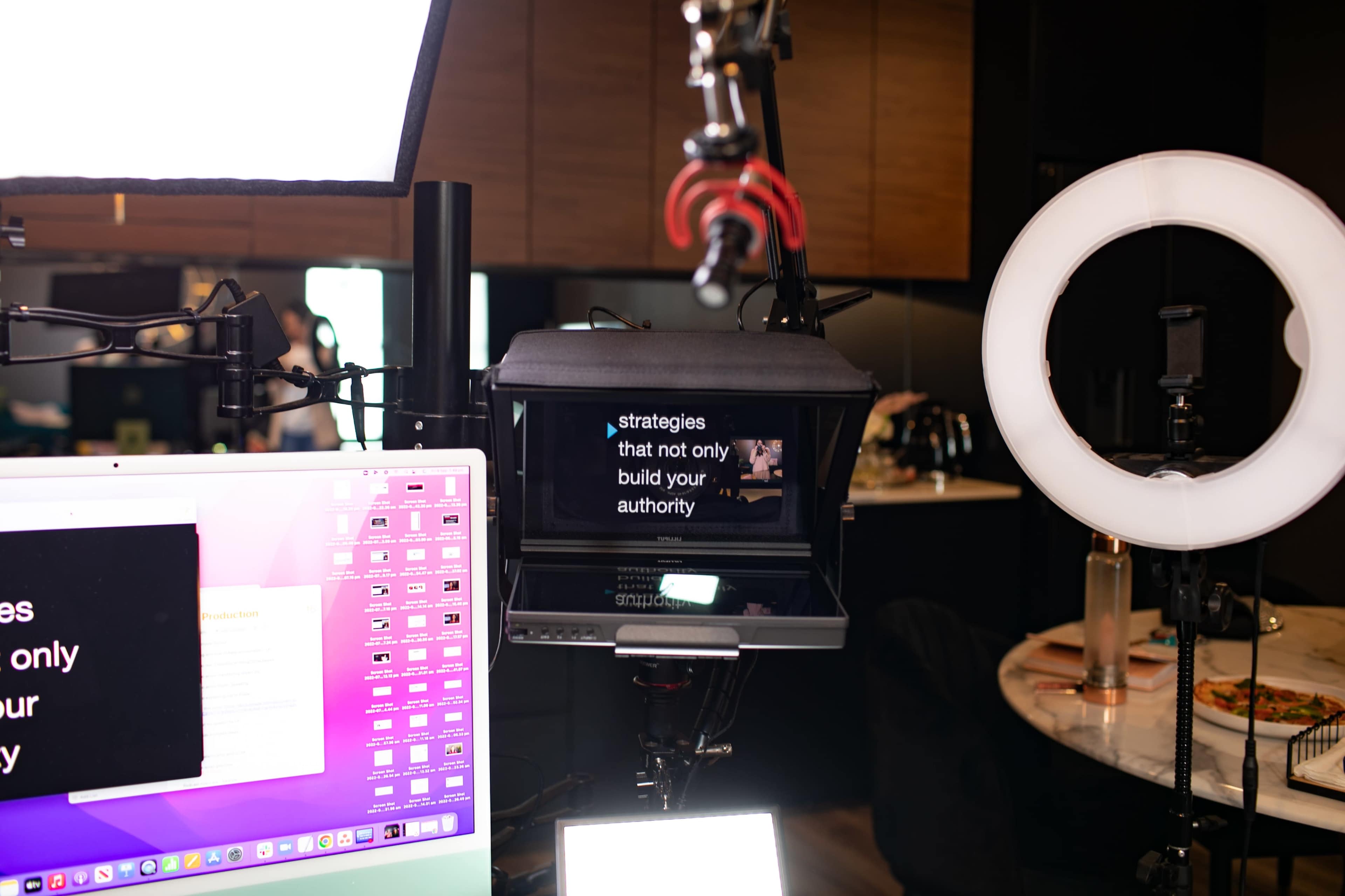 A camera setup displays text on a monitor, with a computer and ring light in the background.