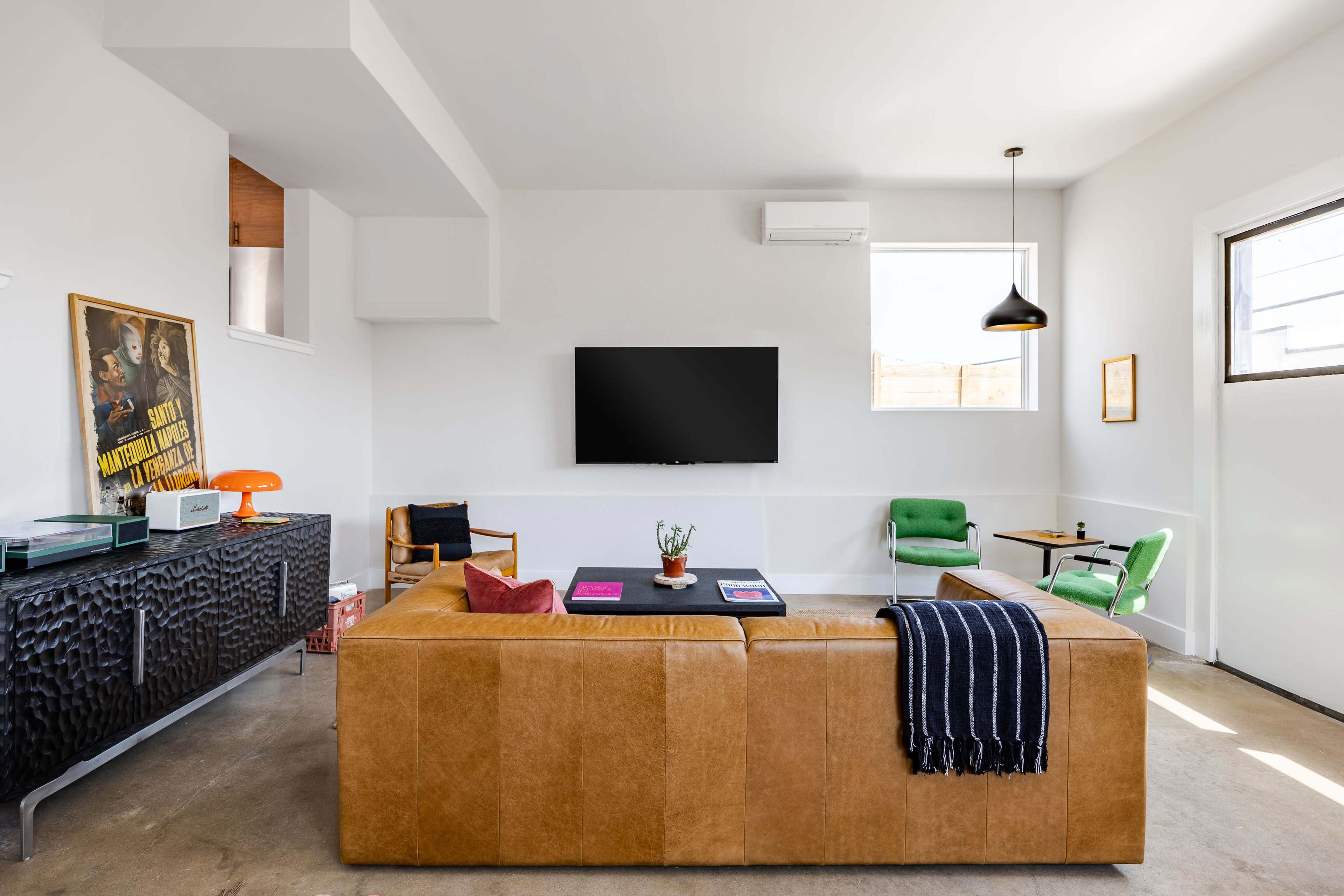 A modern living room with a brown leather sofa, a wall-mounted television, and minimalist furniture, including a green chair and a black sideboard.