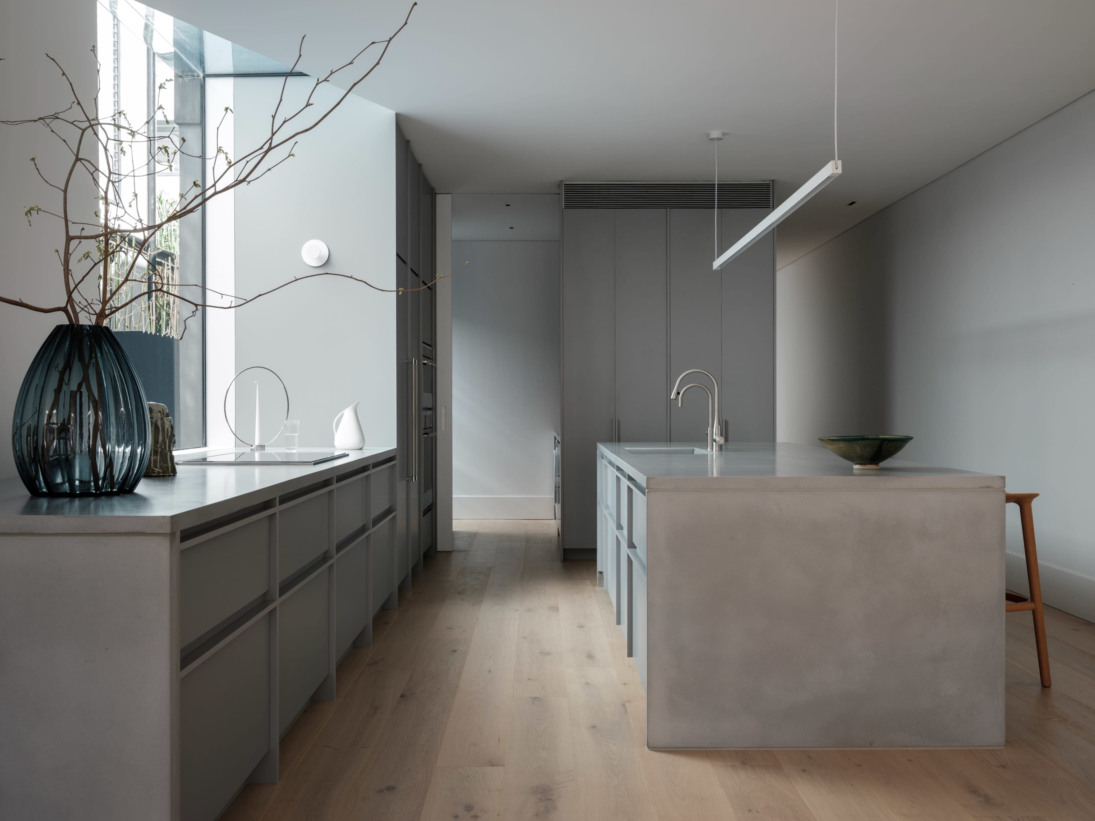 A modern kitchen featuring gray cabinetry, a central island, and minimalist decor with a vase and a small bowl.