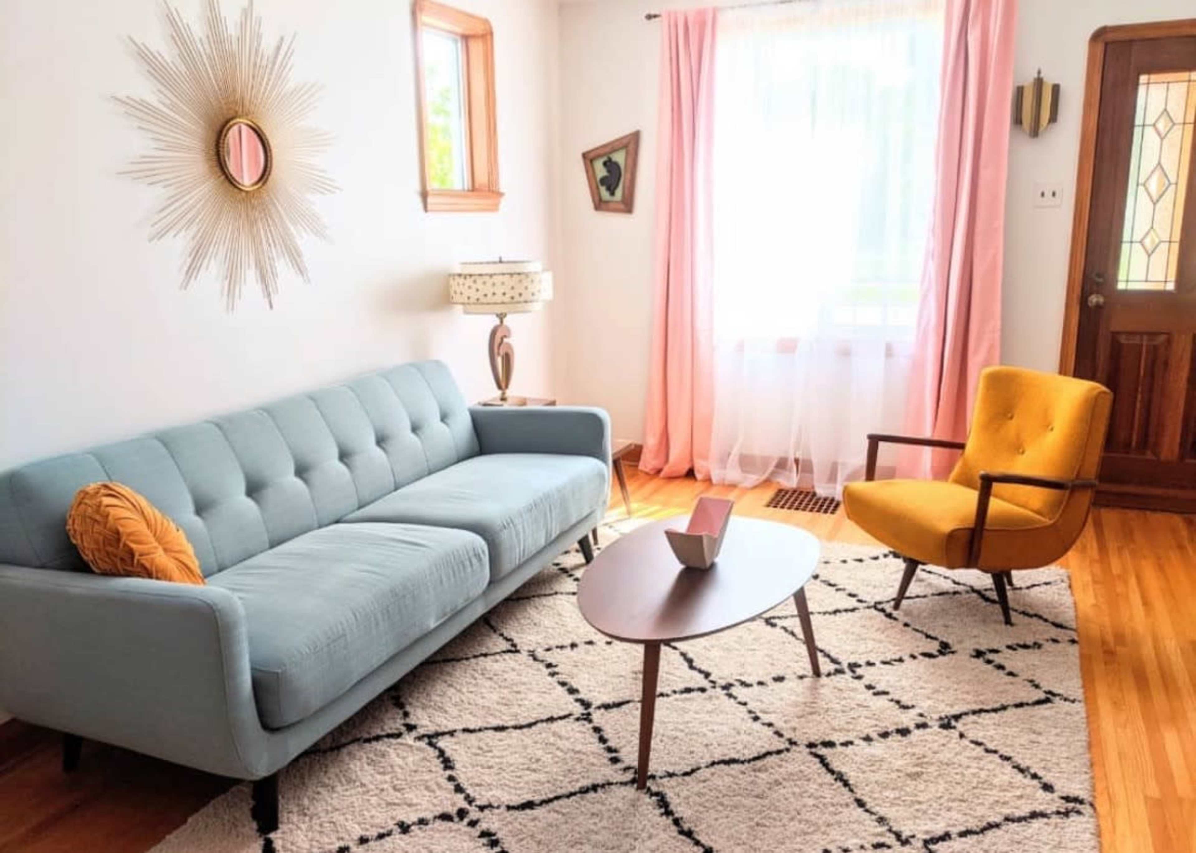 The living room features a light blue couch, a yellow armchair, a round coffee table, and large windows with sheer curtains.