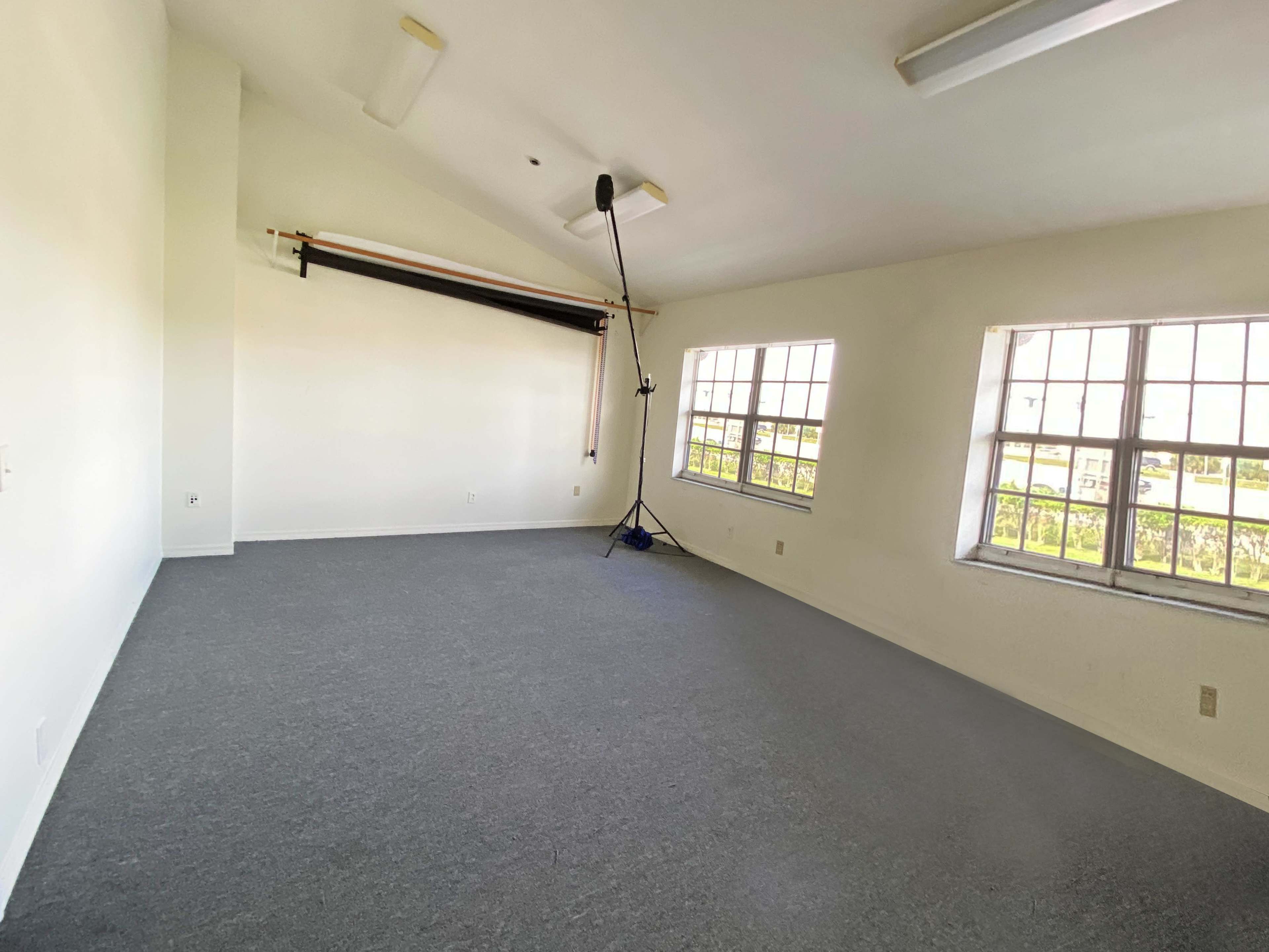 The room features two windows, a gray carpeted floor, and a backdrop support stand mounted on the wall.
