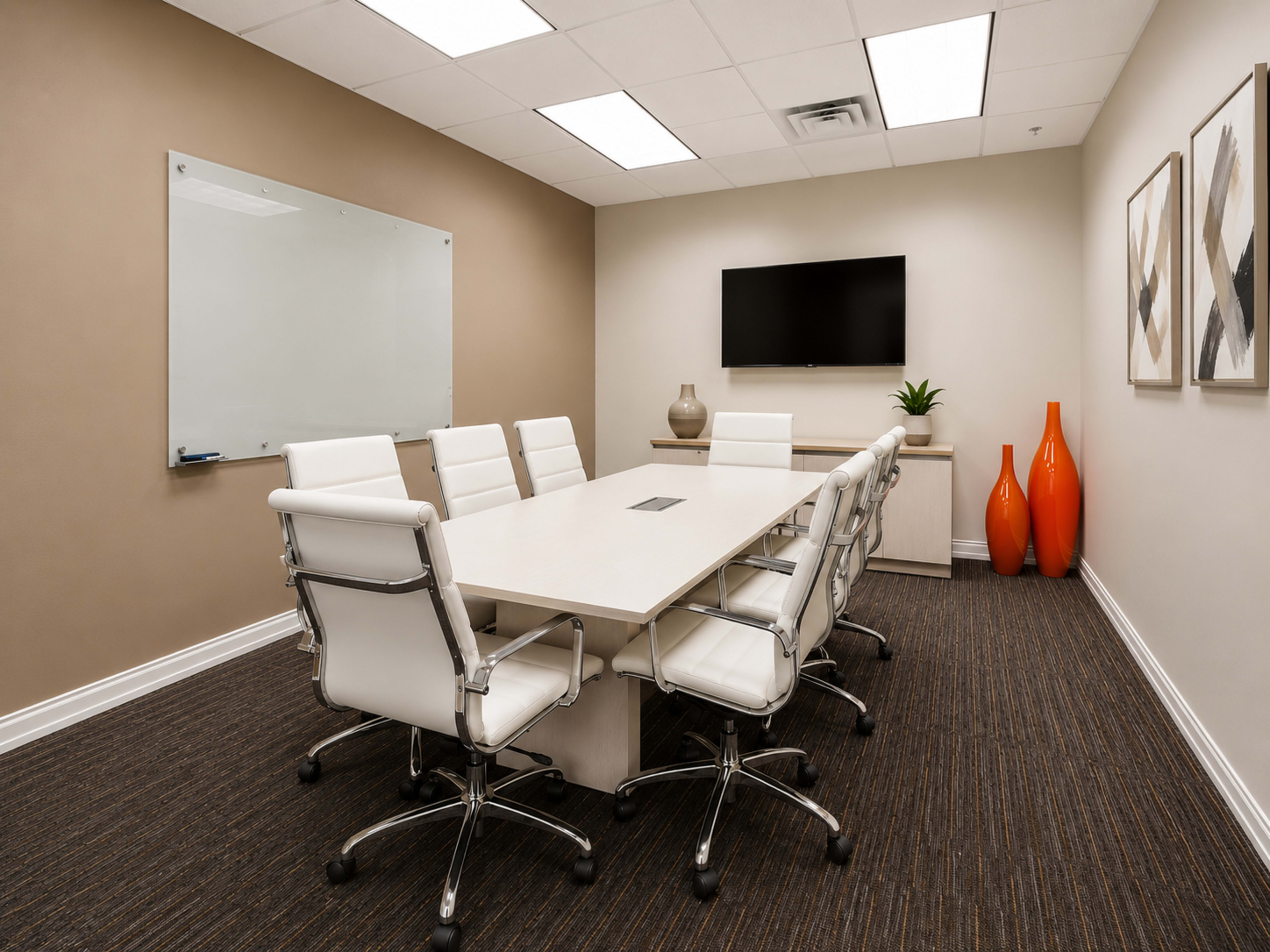 The image shows a modern conference room with a long white table surrounded by eight white chairs, a wall-mounted TV, a large whiteboard, and decorative orange vases.