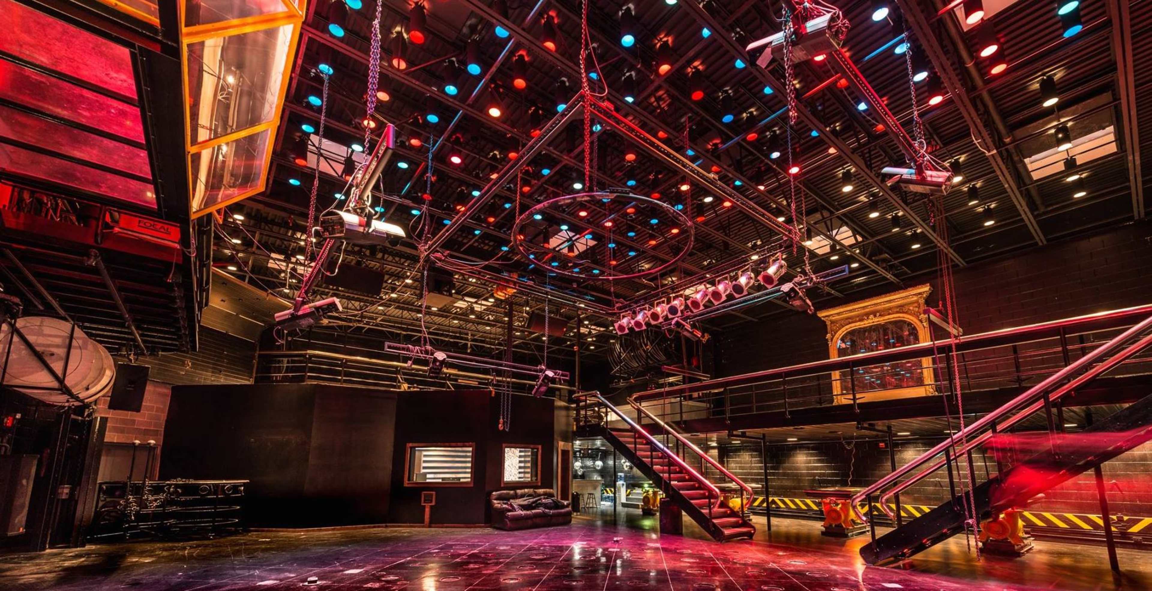A large, empty performance space featuring a grid of overhead lights and a multi-level seating area with a glossy floor.