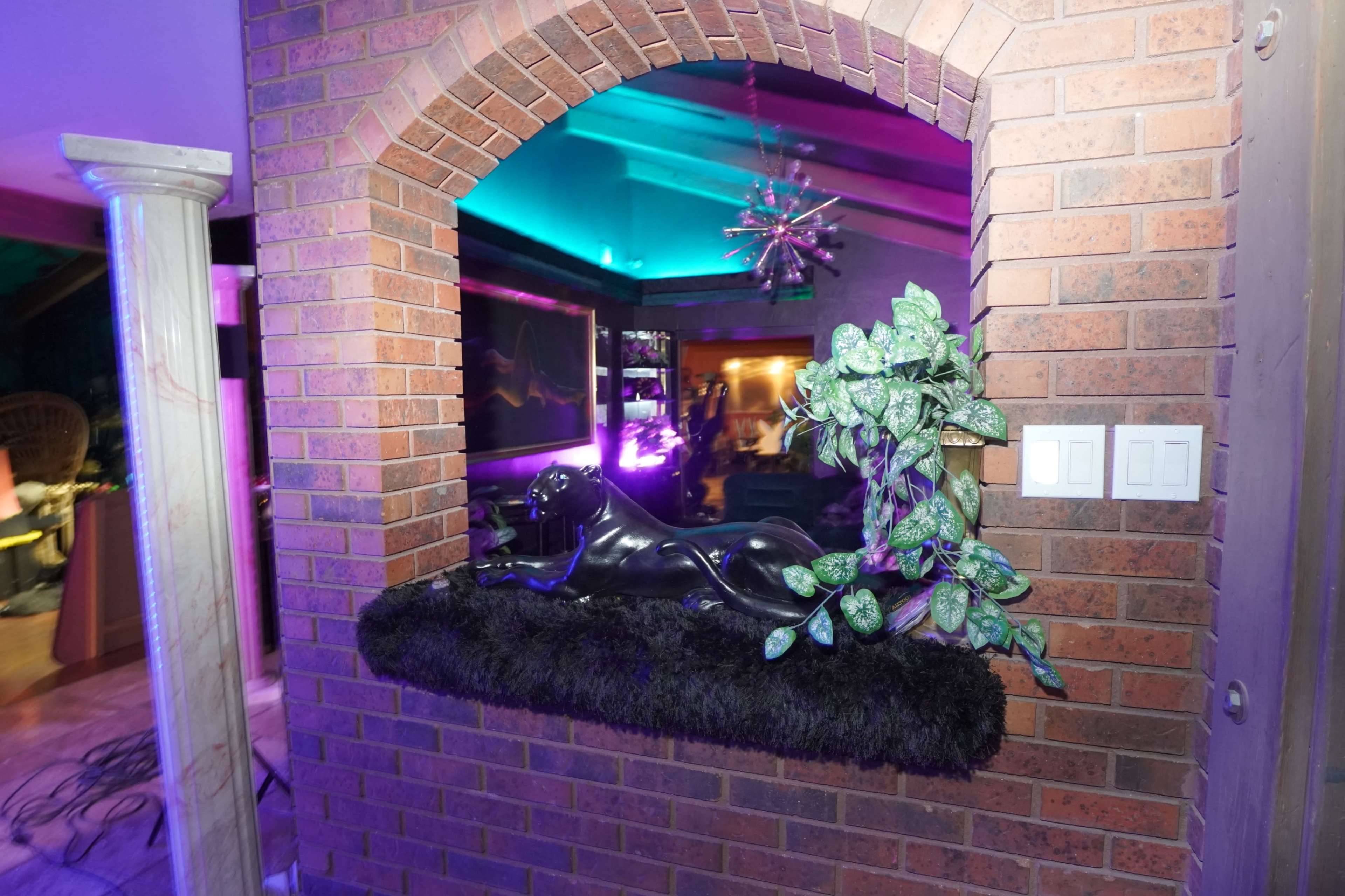 A black panther statue lies on a fur-covered surface within an arched brick opening, illuminated by colorful lights in the background.