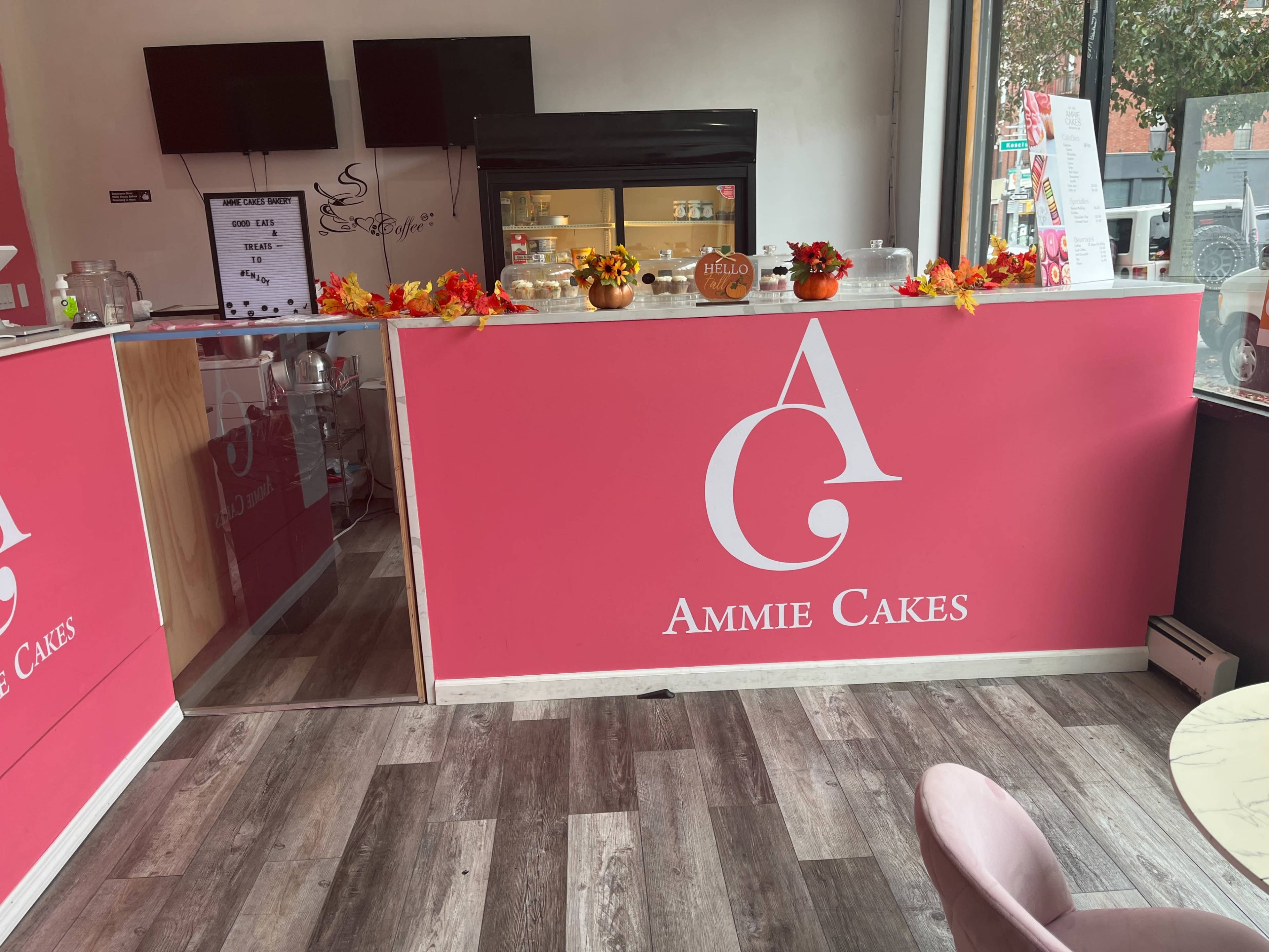 The interior of a bakery named "Ammie Cakes," featuring a pink counter with seasonal decorations and a glass display case in the background.
