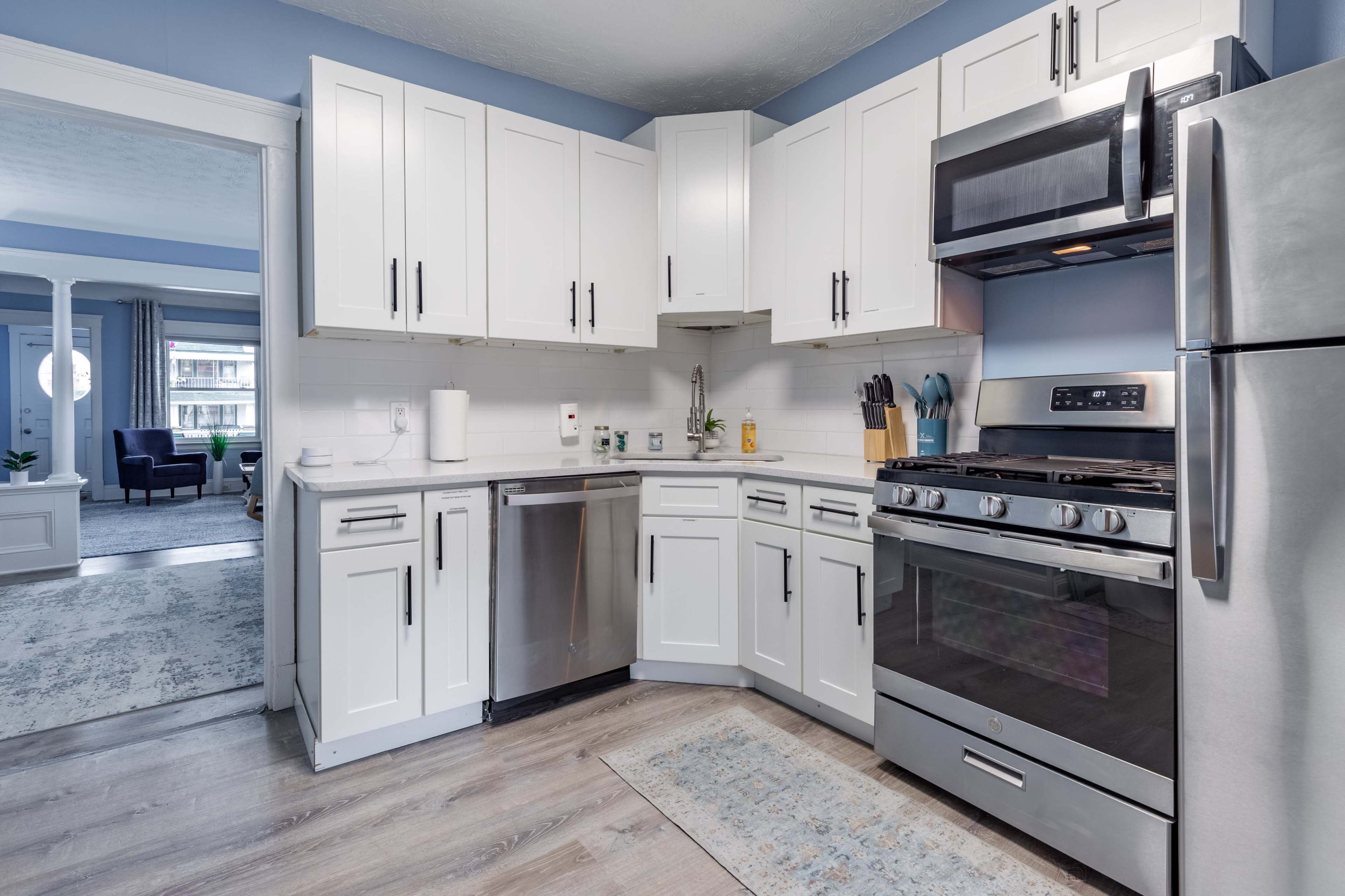 A modern kitchen features white cabinetry, stainless steel appliances, and a light-colored floor with a rug.