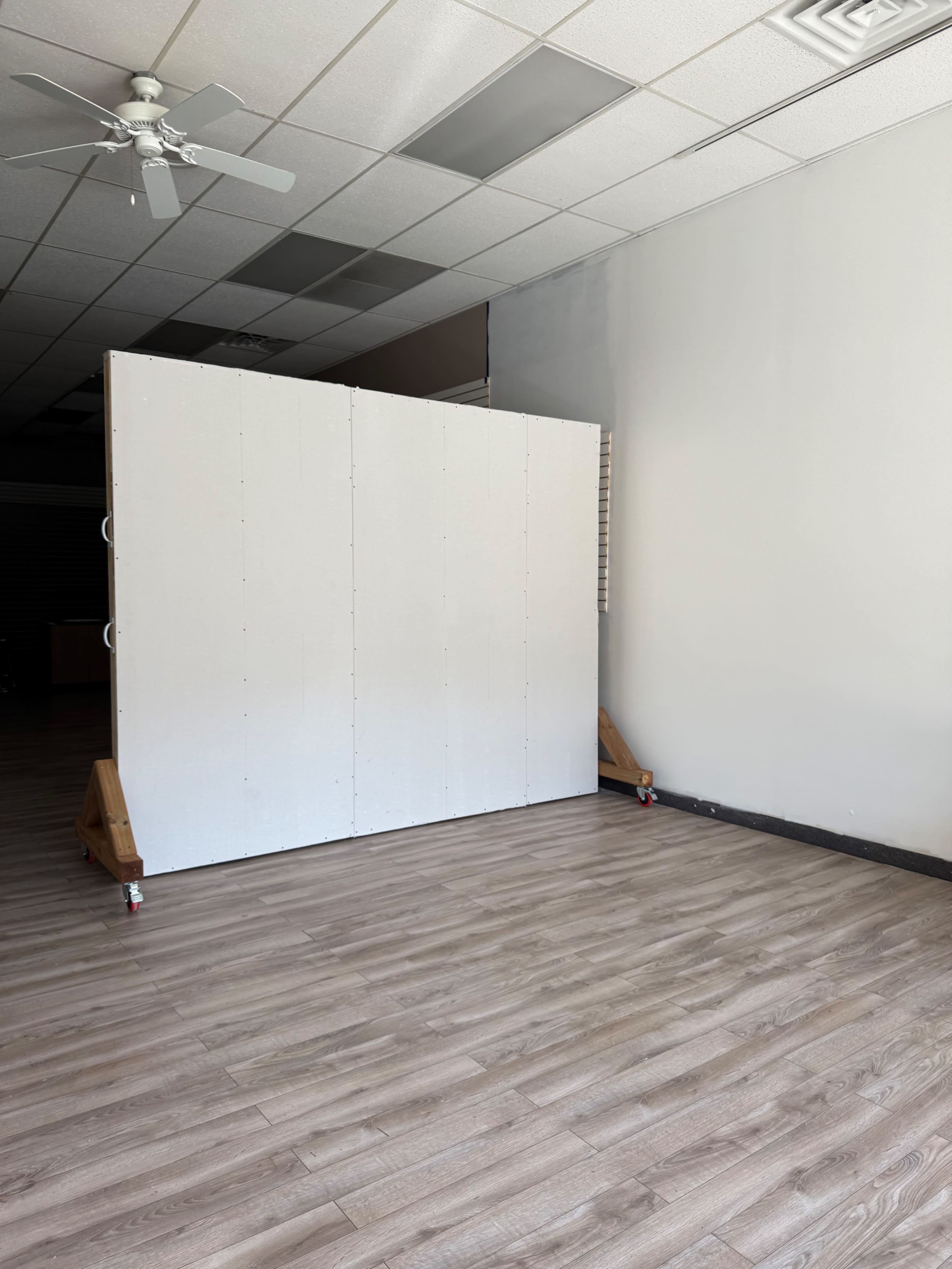 The image shows a spacious interior with a wooden floor and a large white partition occupying the center of the room.