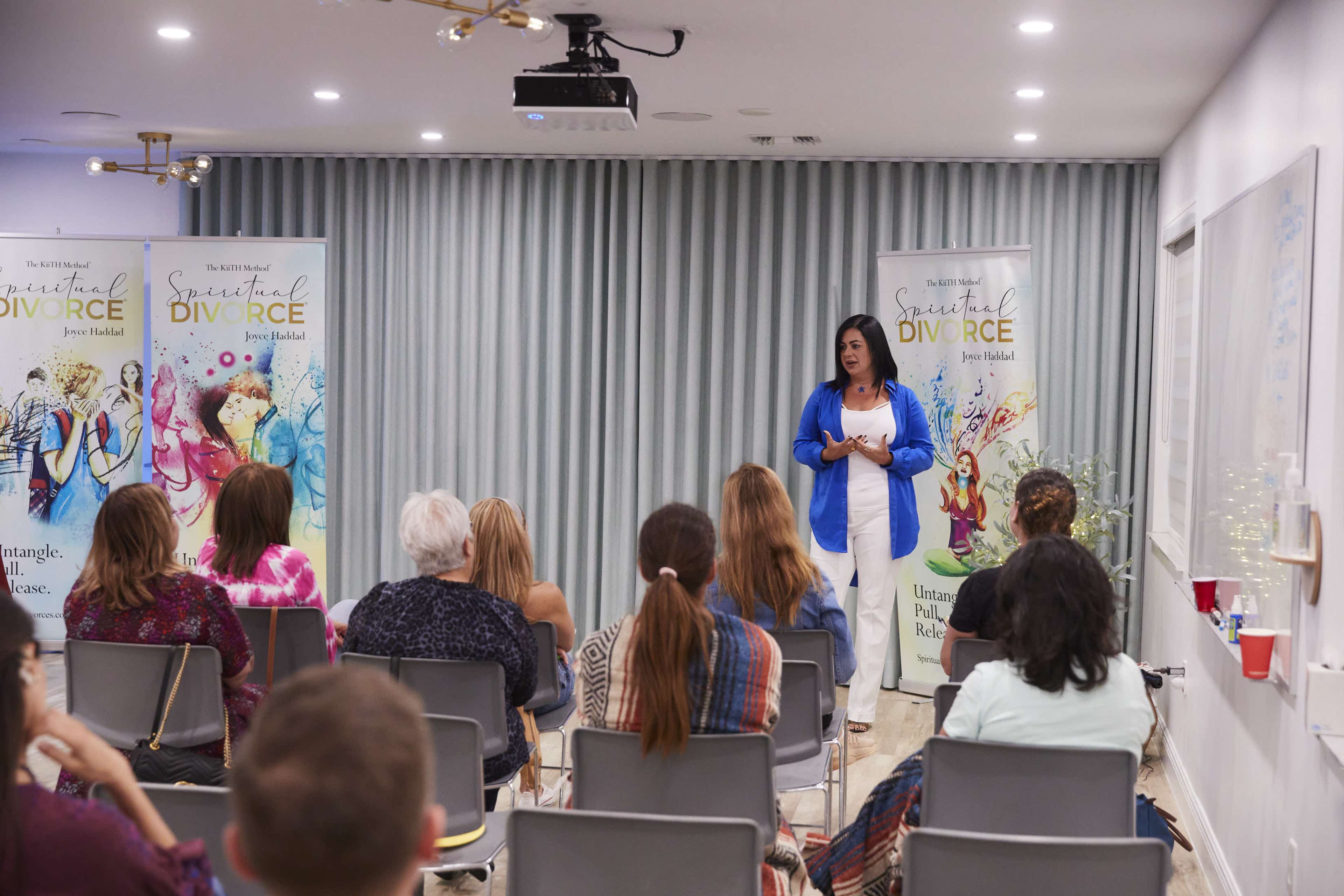 A woman speaks to an audience in a room decorated with banners about spiritual divorce.