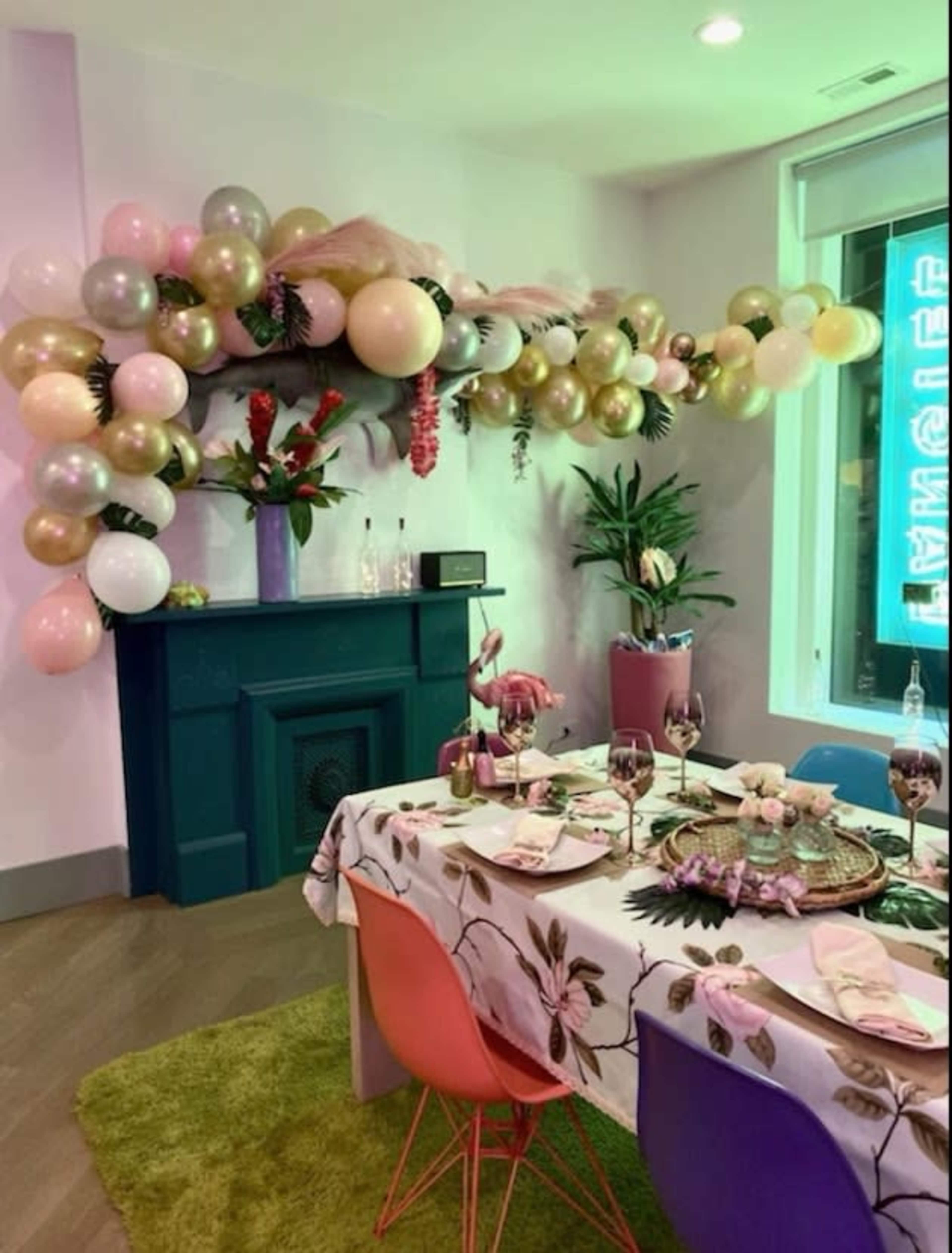 A dining area features a table set with decorative tableware under a balloon arrangement and a floral centerpiece.